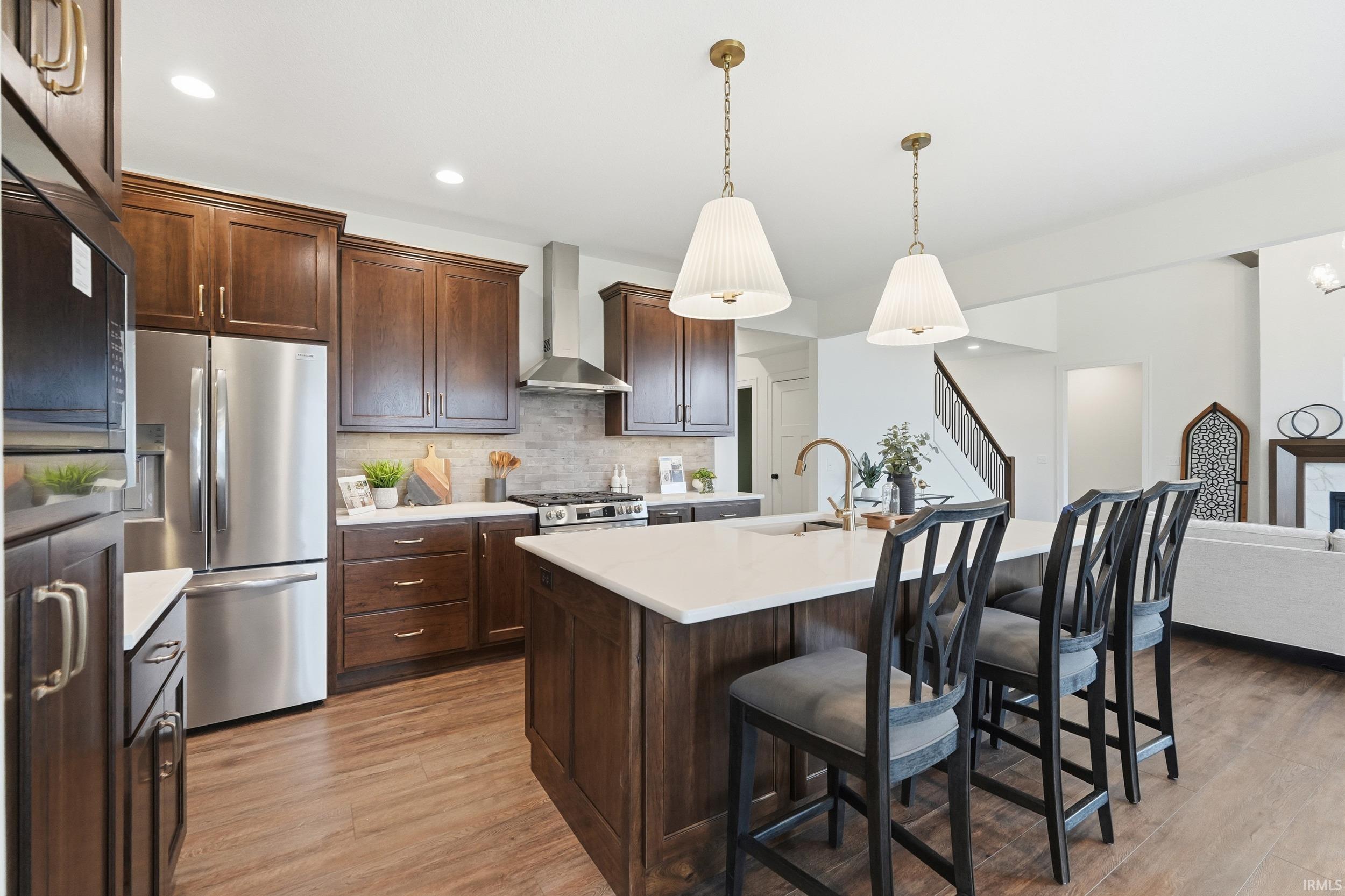 Kitchen featuring appliances with stainless steel finishes, a kitchen bar, light wood finished floors, wall chimney exhaust hood, and backsplash