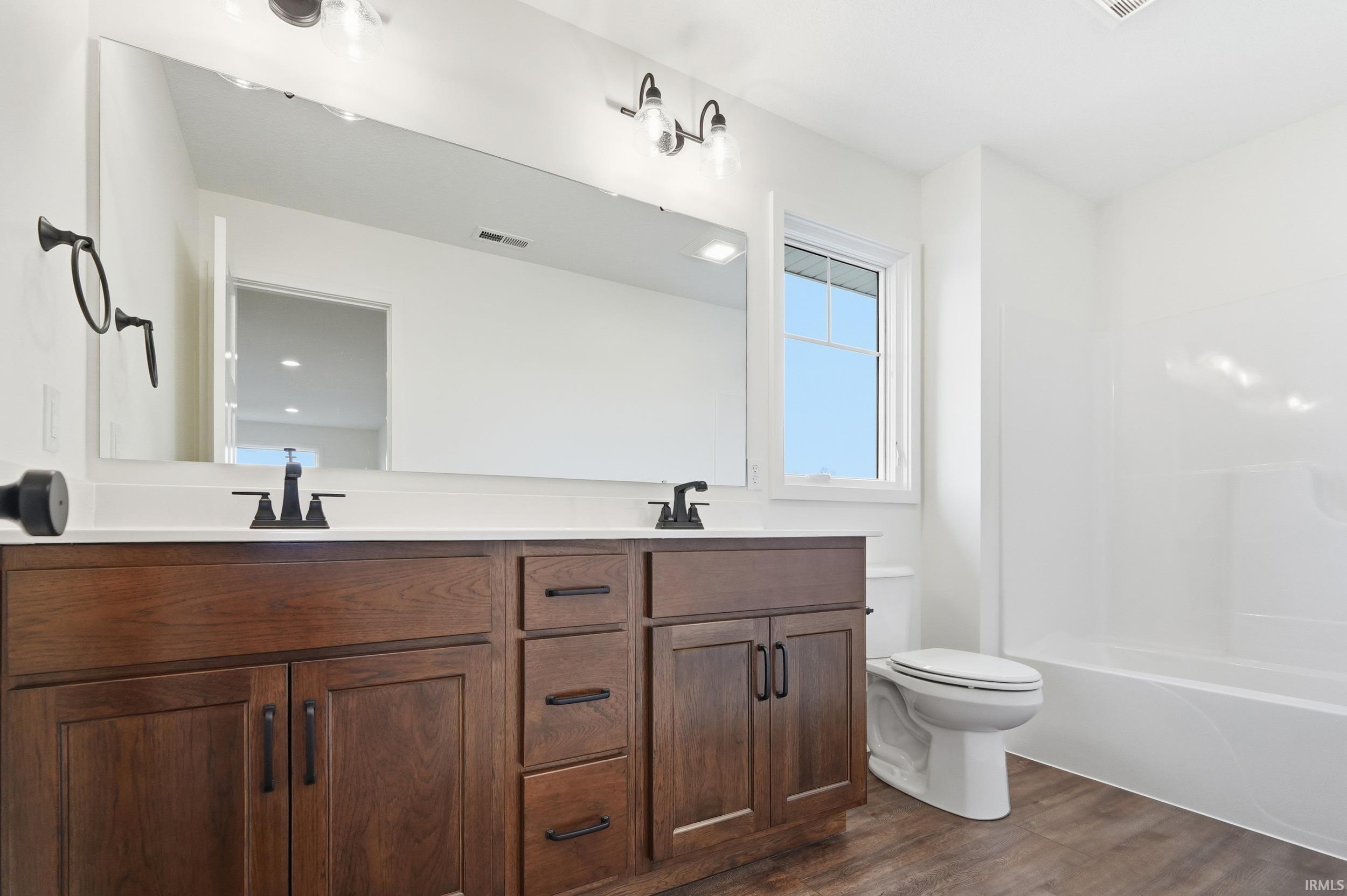 Bathroom with double vanity, dark wood-type flooring, and shower / washtub combination