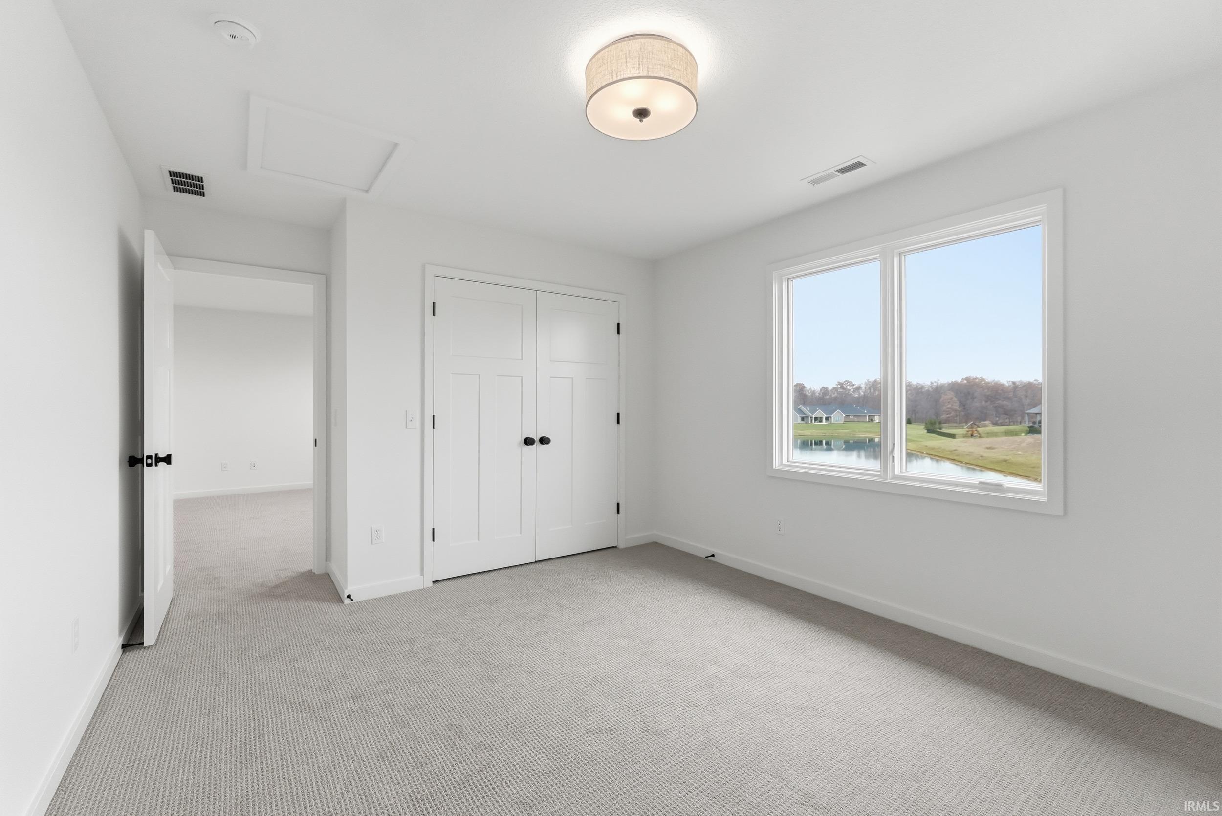 Unfurnished bedroom with light carpet, attic access, a closet, and a water view