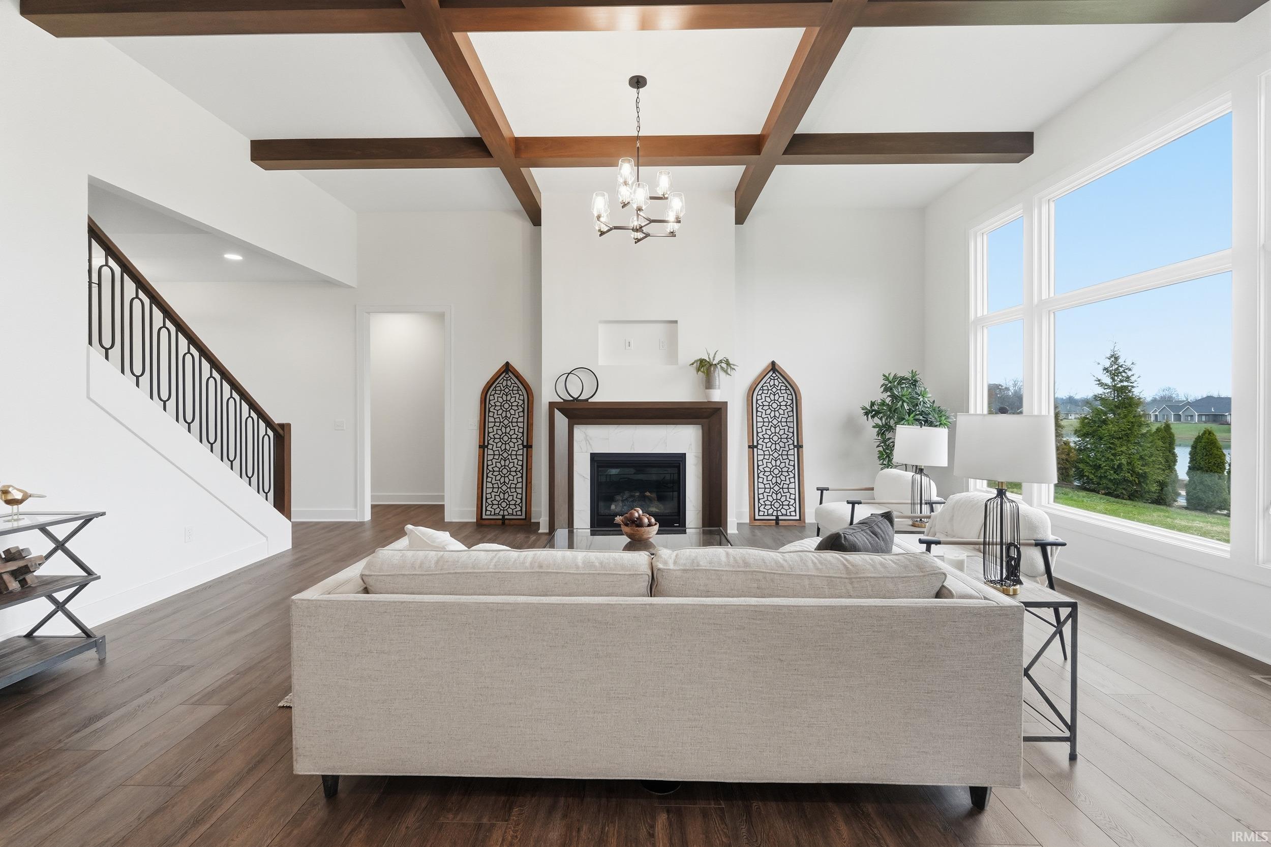 Living room featuring coffered ceiling, beamed ceiling, a glass covered fireplace, wood finished floors, and a chandelier