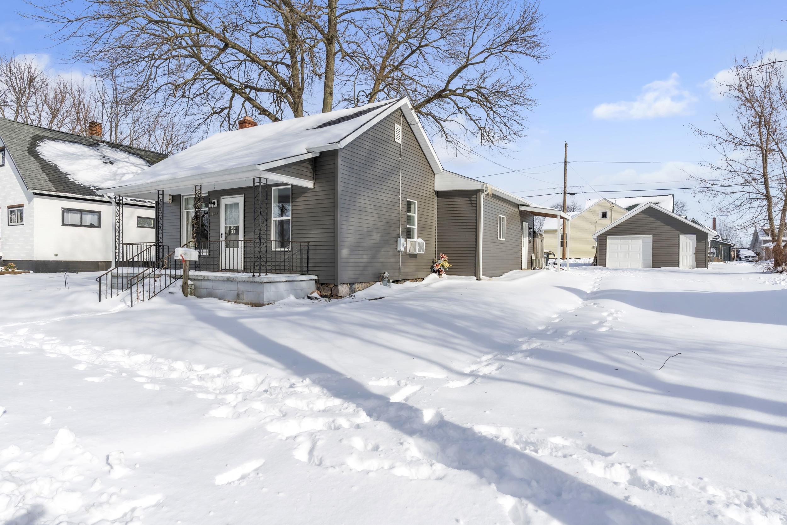 View of snowy exterior with a chimney, a detached garage, and an outbuilding