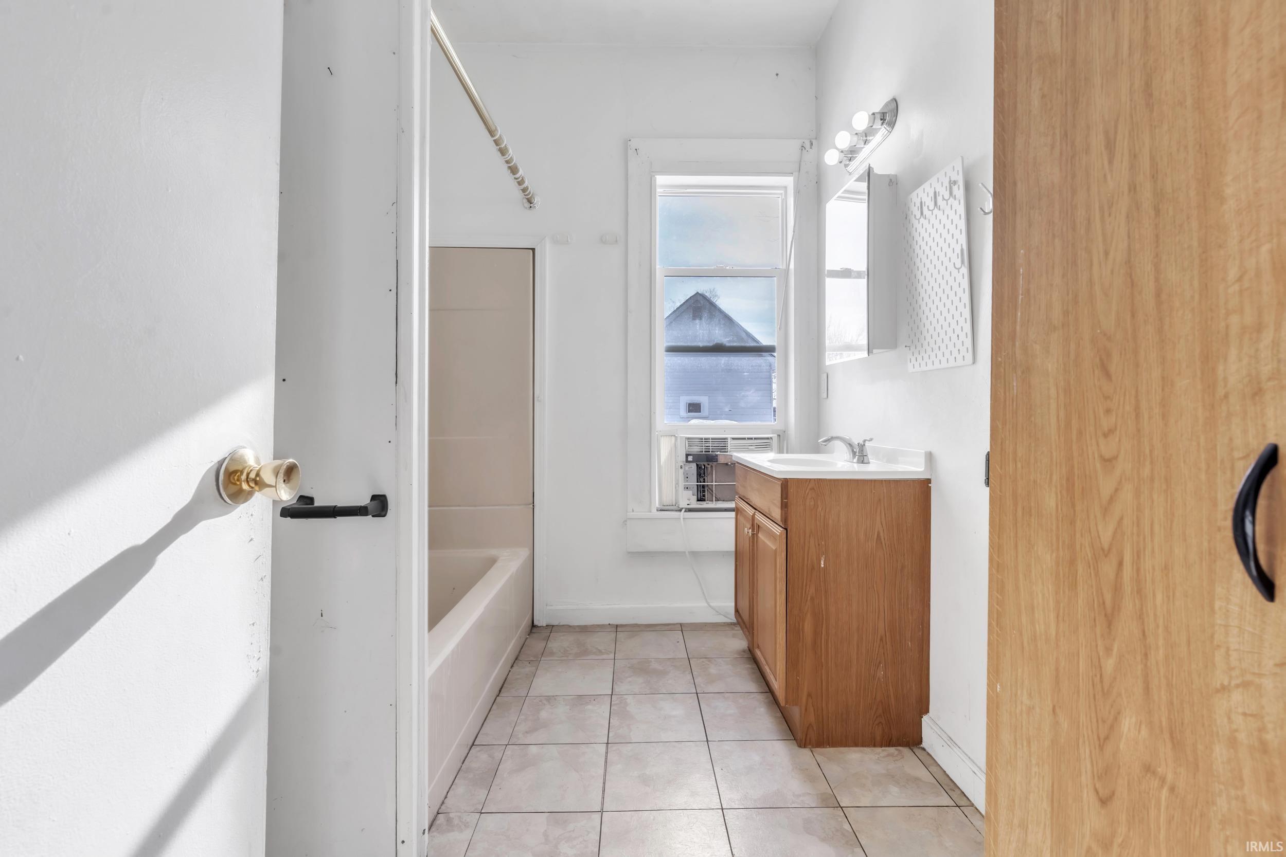 Full bath featuring vanity, light tile patterned flooring, and washtub / shower combination