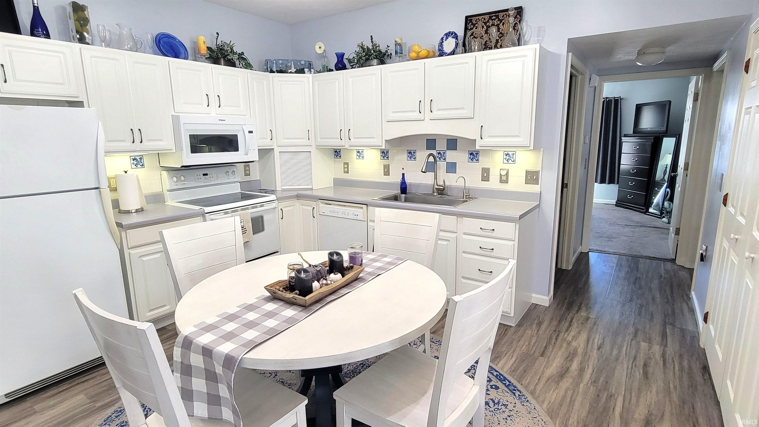 Kitchen with white appliances, white cabinets, dark wood-style flooring, light countertops, and backsplash
