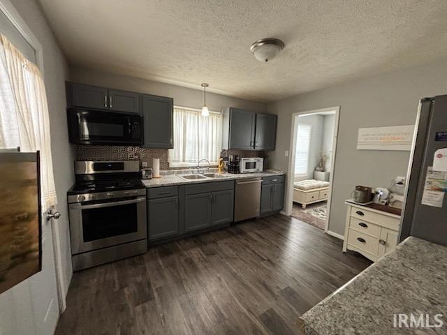 Kitchen with stainless steel appliances, a textured ceiling, gray cabinets, dark wood-type flooring, and pendant lighting