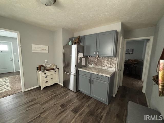 Kitchen featuring gray cabinets, a textured ceiling, freestanding refrigerator, tasteful backsplash, and dark wood-style flooring