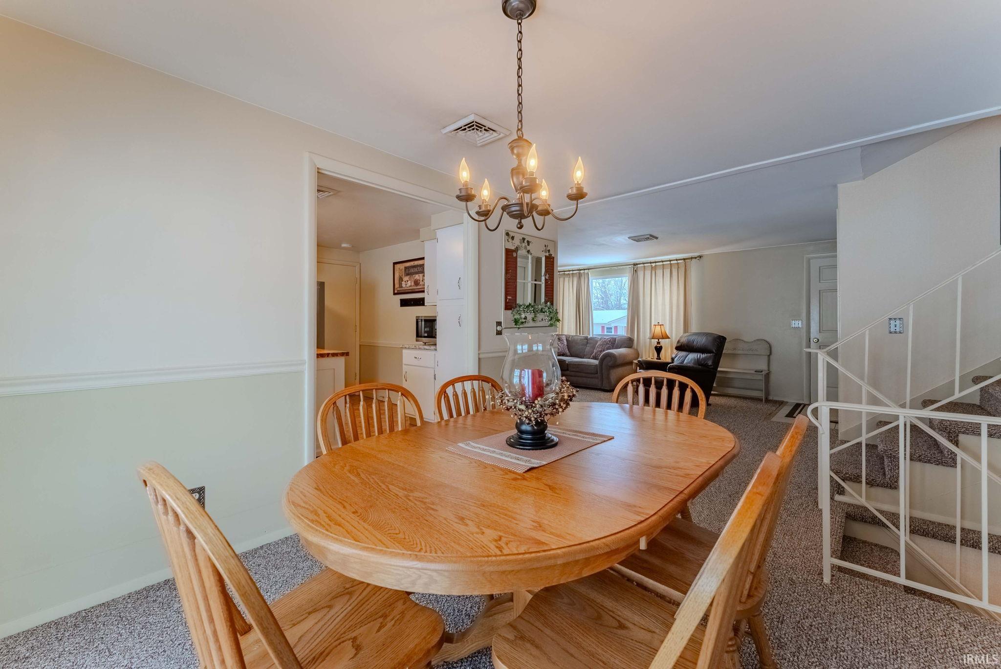 Dining room with stairs, carpet flooring, and a chandelier