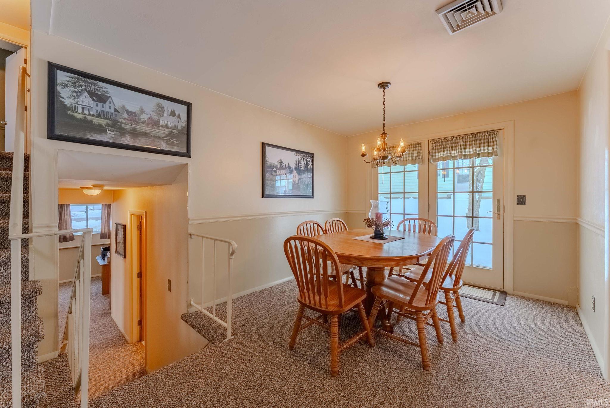 Carpeted dining space featuring stairs and a chandelier