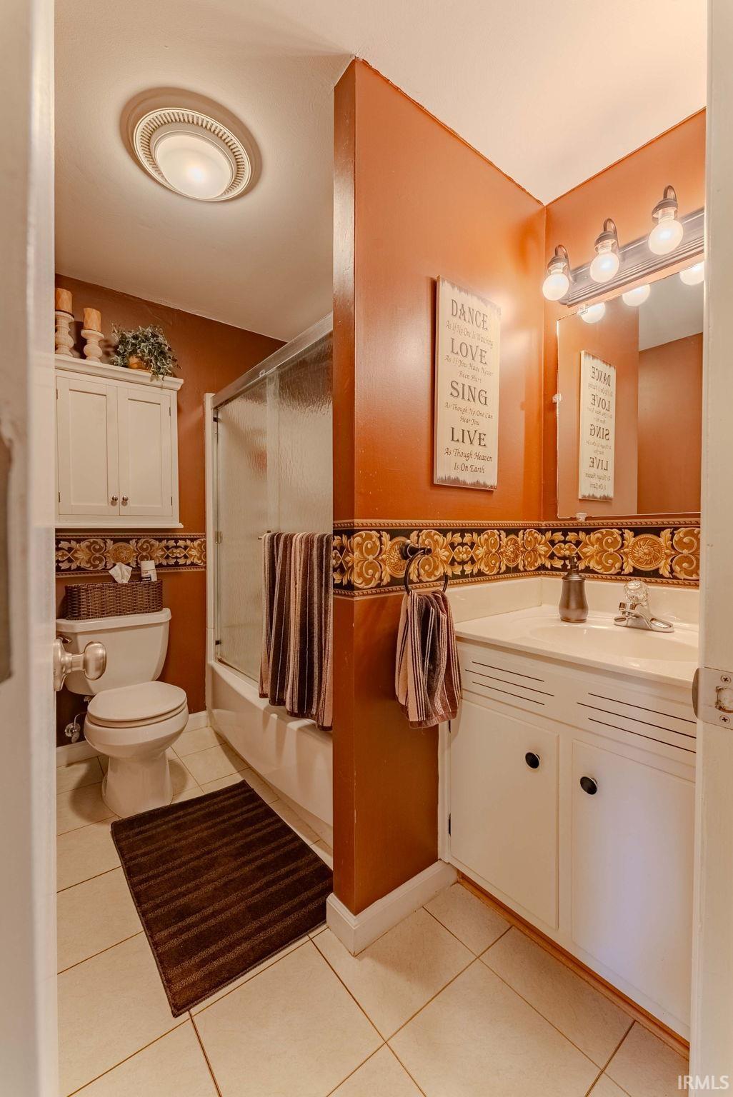 Bathroom featuring vanity, shower / bath combination with glass door, and light tile patterned flooring
