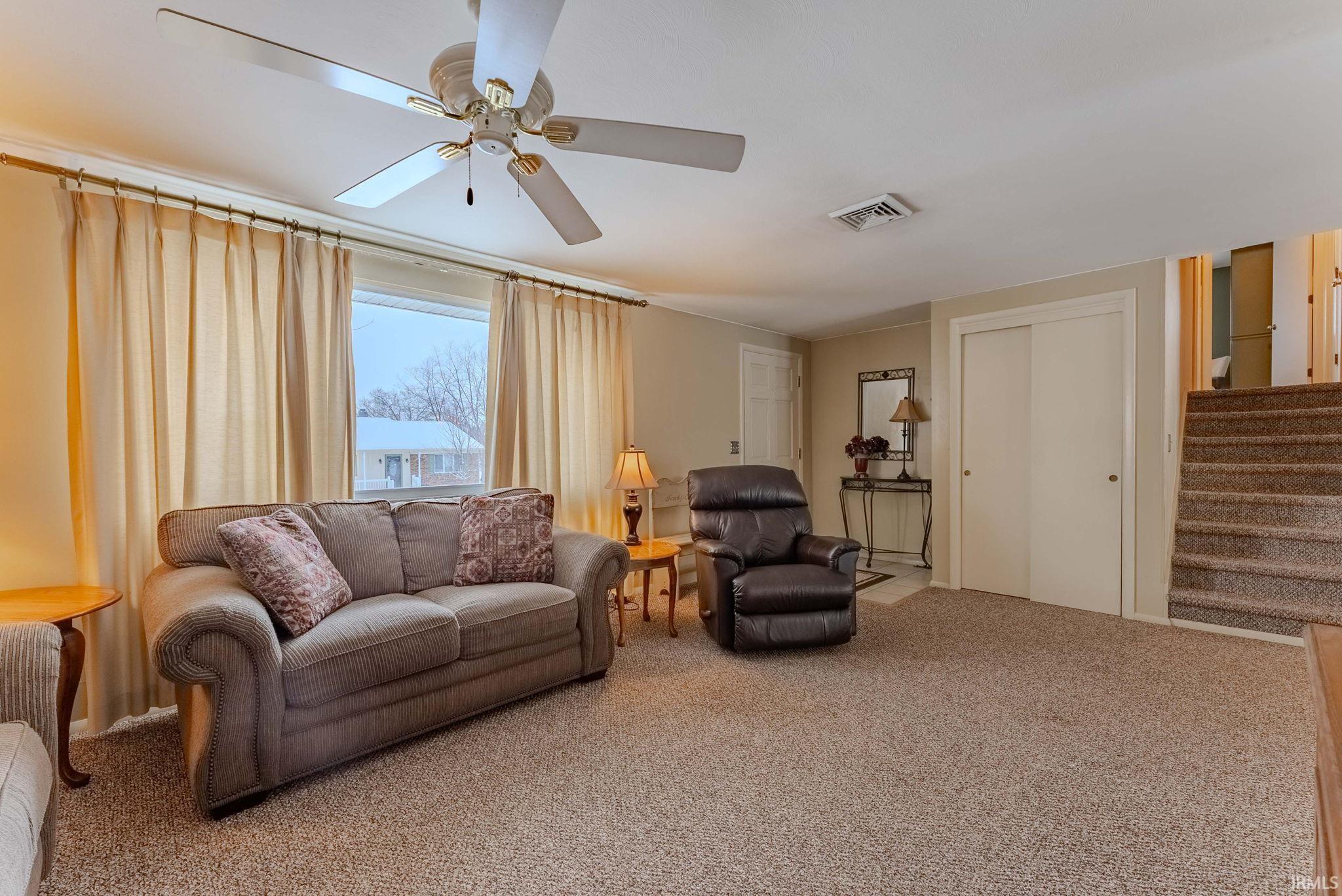 Living area with carpet flooring, stairs, and ceiling fan