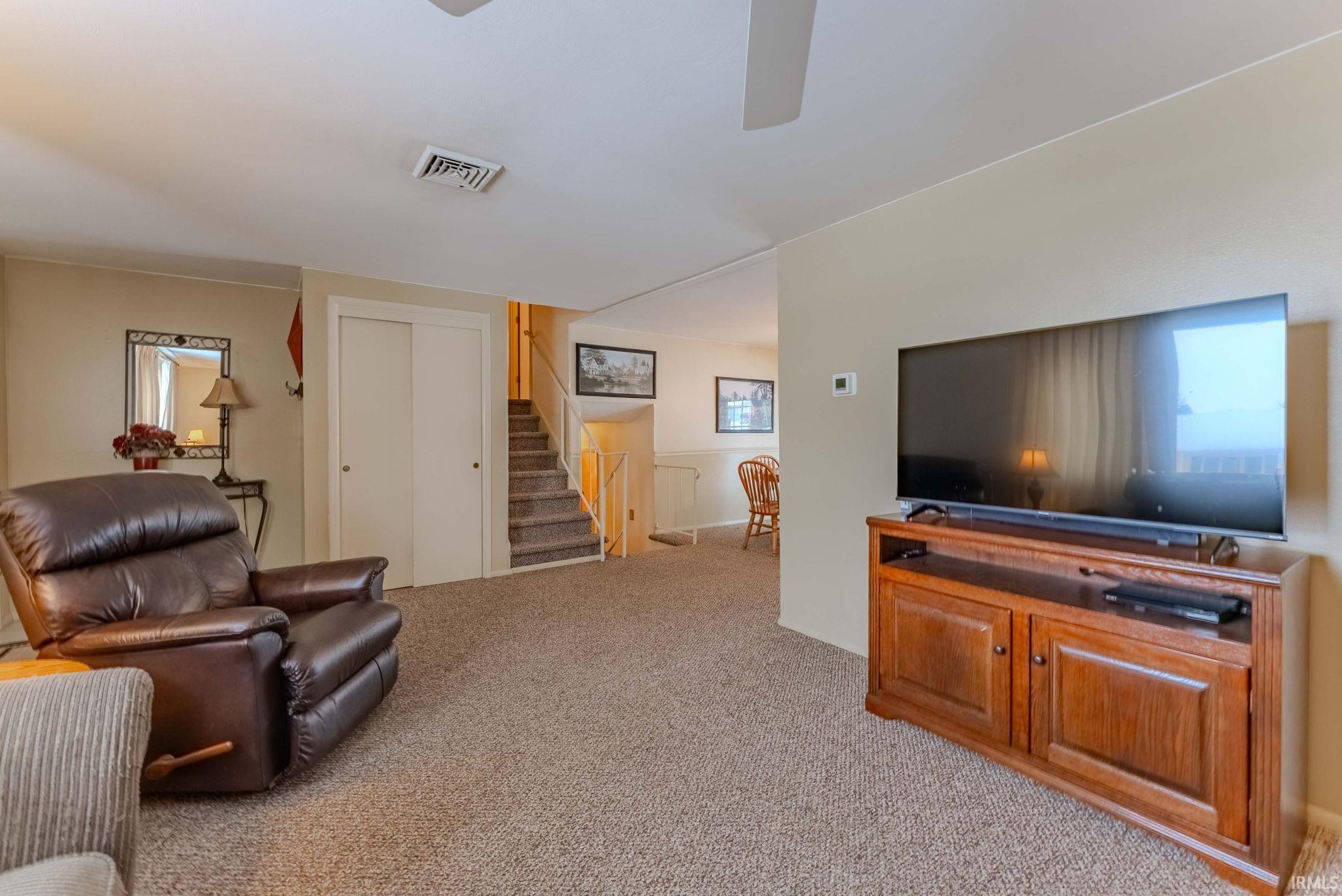 Living room featuring light colored carpet, stairs, and ceiling fan