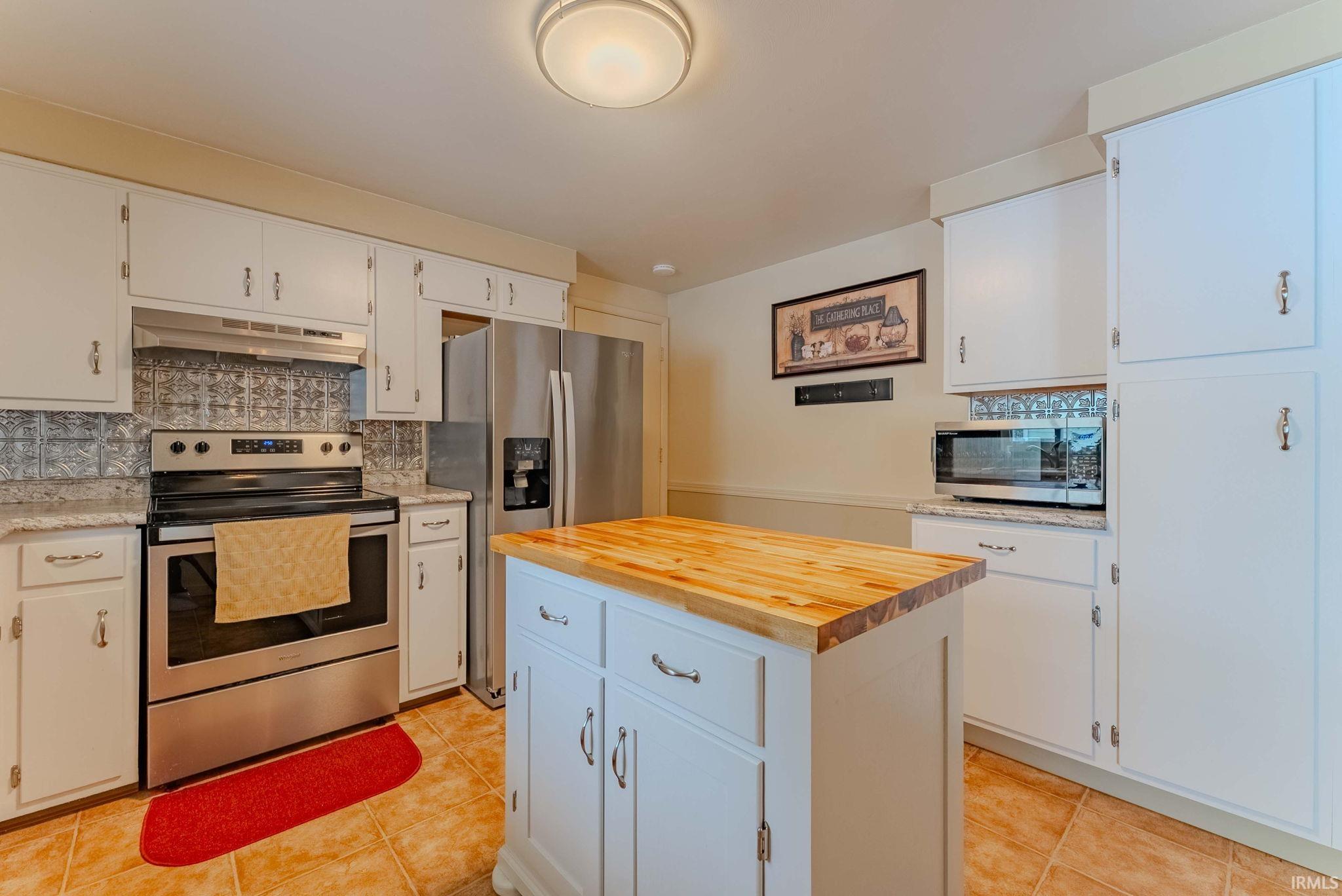 Kitchen featuring appliances with stainless steel finishes, butcher block counters, tasteful backsplash, and white cabinetry