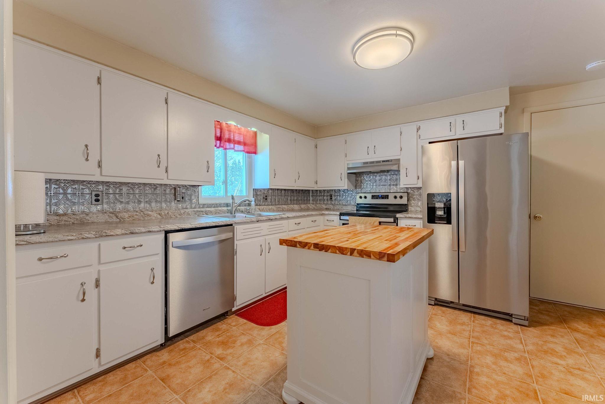 Kitchen featuring appliances with stainless steel finishes, wood counters, white cabinets, decorative backsplash, and a kitchen island