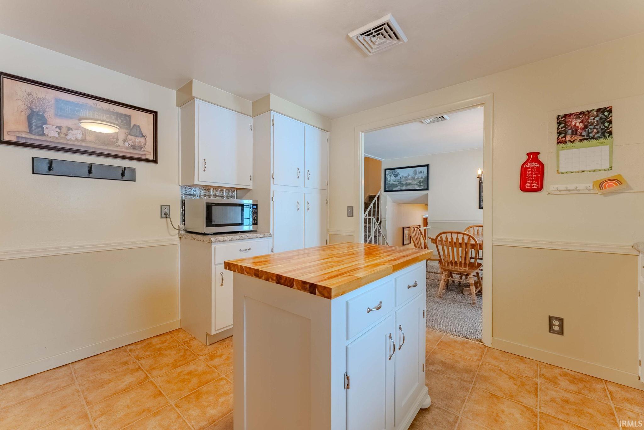 Kitchen featuring wood counters, white cabinets, stainless steel microwave, a kitchen island, and light tile patterned flooring