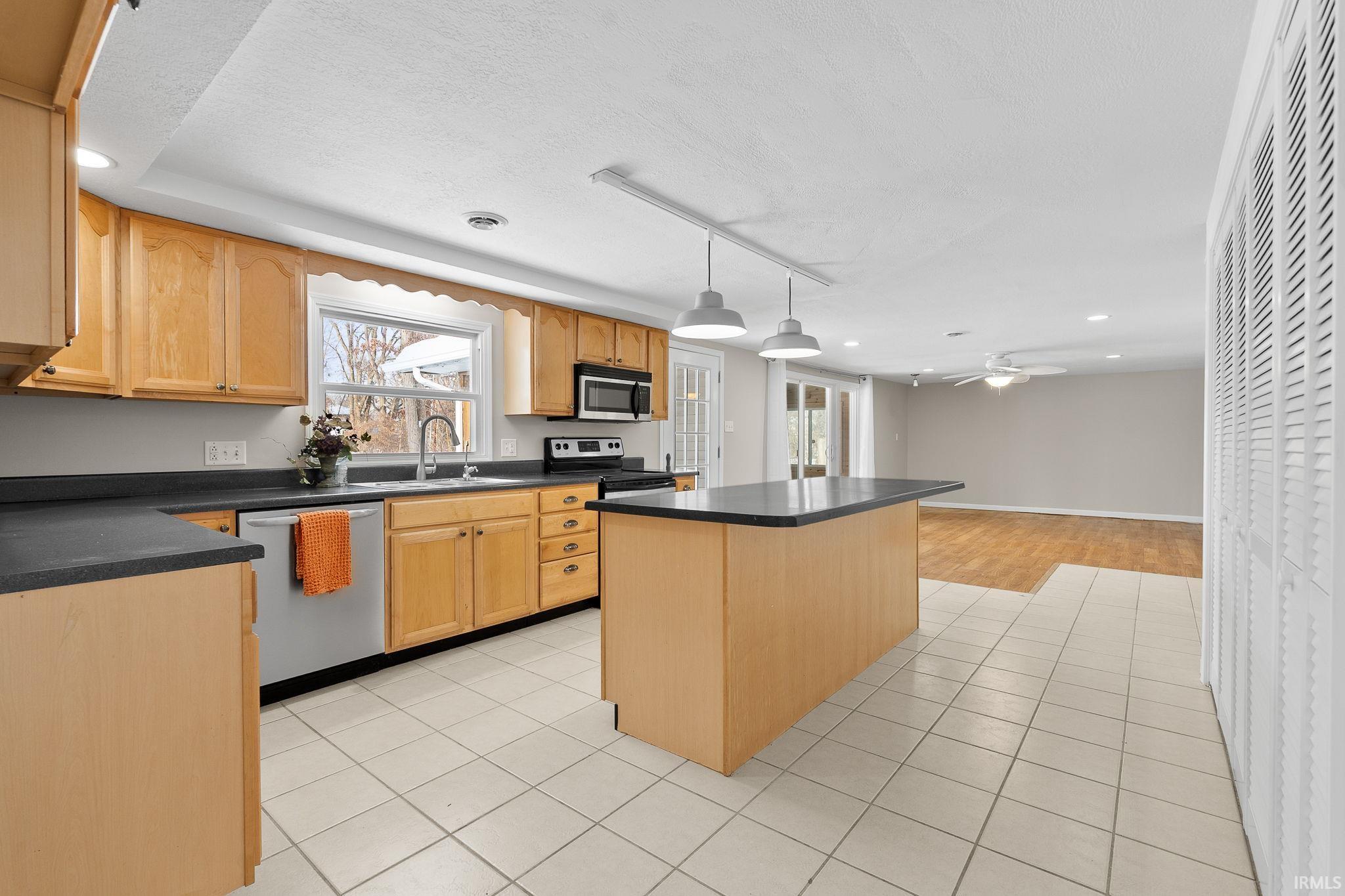 Kitchen featuring recessed lighting, dark countertops, a kitchen island, appliances with stainless steel finishes, and hanging light fixtures