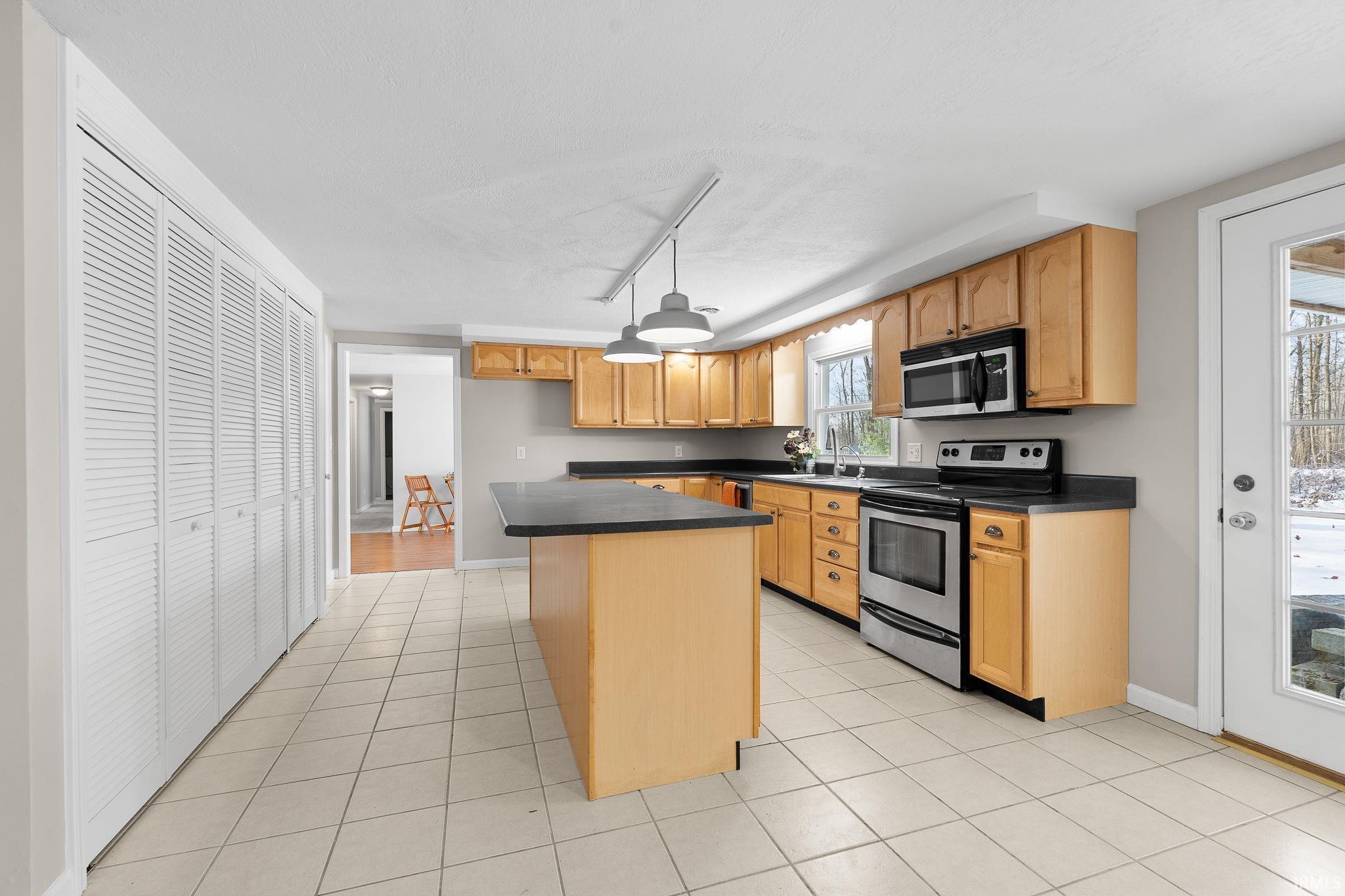 Kitchen featuring appliances with stainless steel finishes, dark countertops, a center island, light tile patterned flooring, and light brown cabinets