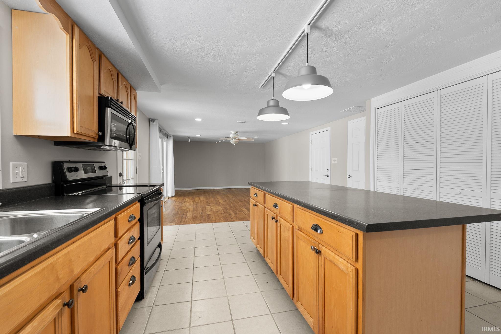 Kitchen with electric range, dark countertops, hanging light fixtures, rail lighting, and light tile patterned floors