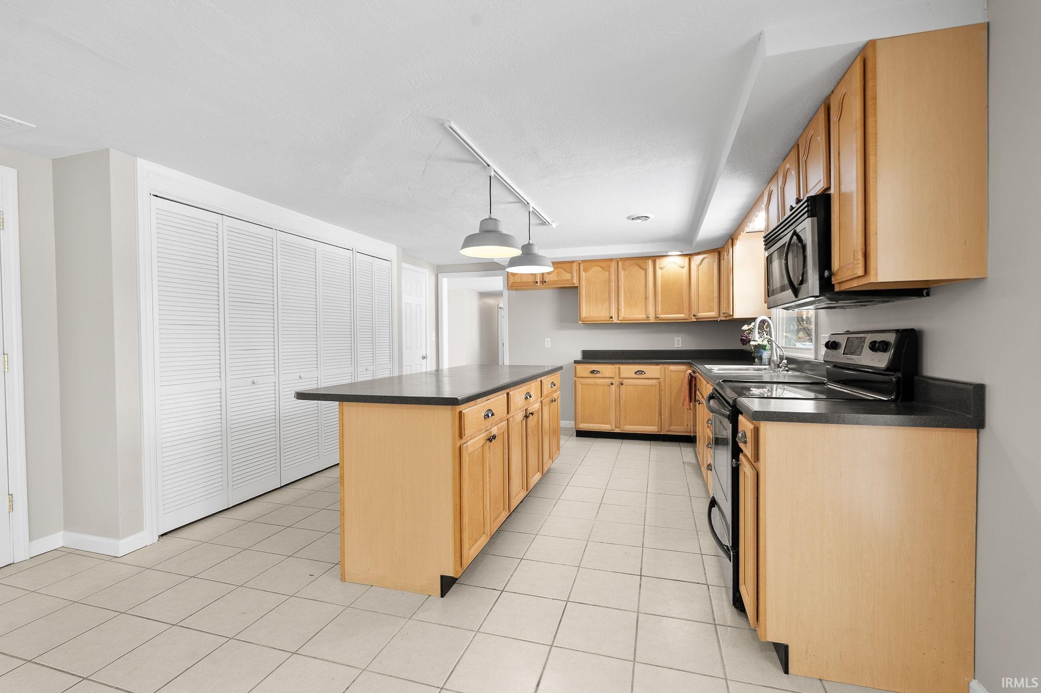 Kitchen featuring electric range, dark countertops, track lighting, light brown cabinets, and light tile patterned flooring