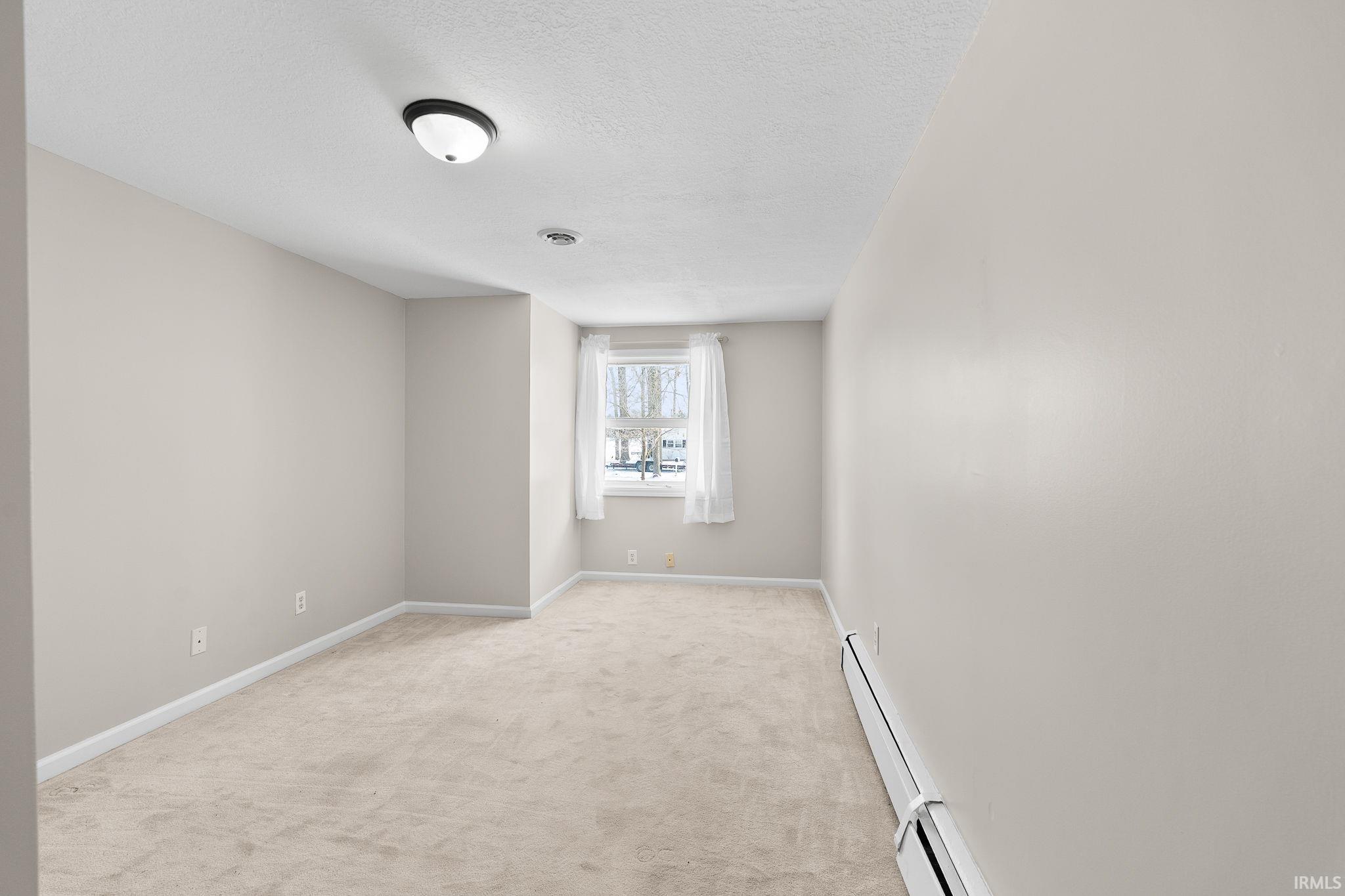Empty room featuring light carpet, a textured ceiling, and baseboard heating