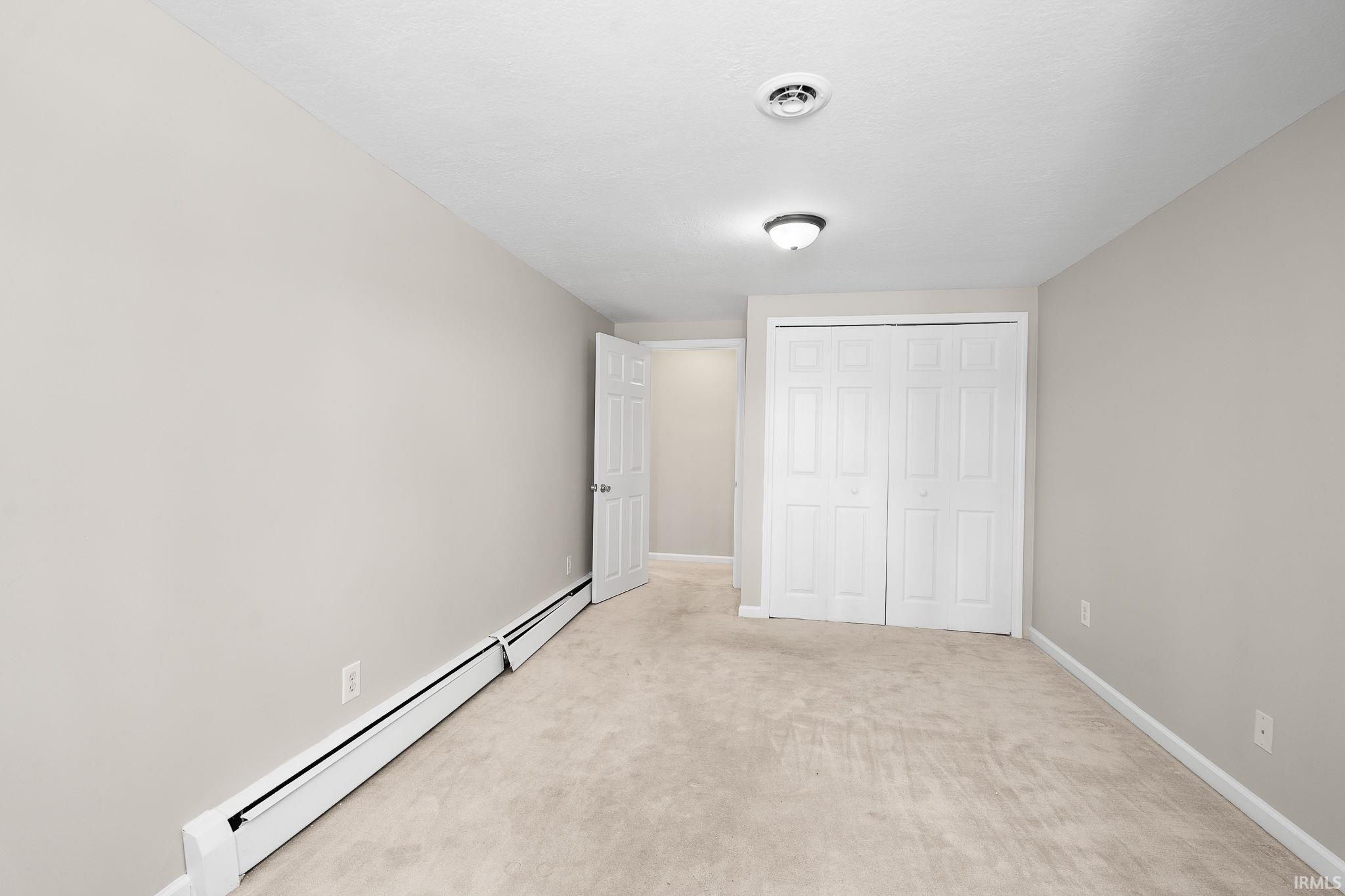 Unfurnished bedroom featuring a baseboard heating unit, light colored carpet, and a closet