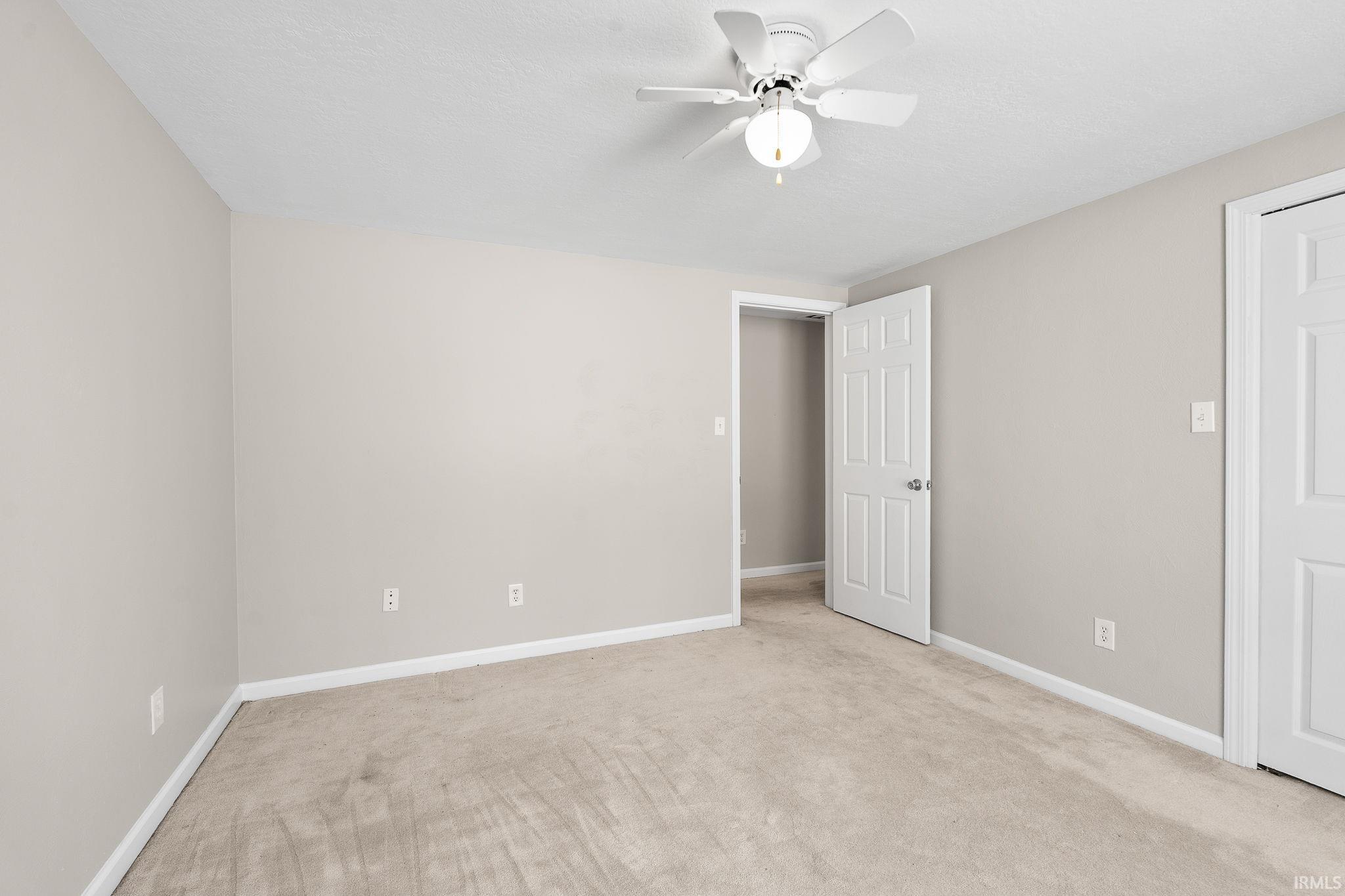 Unfurnished bedroom with light carpet and a ceiling fan