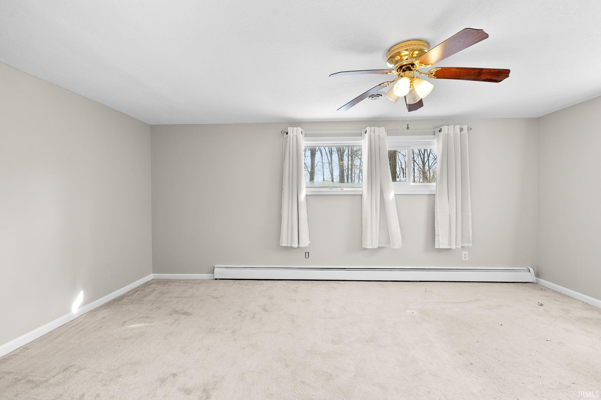 Spare room with light carpet, ceiling fan, and a baseboard radiator