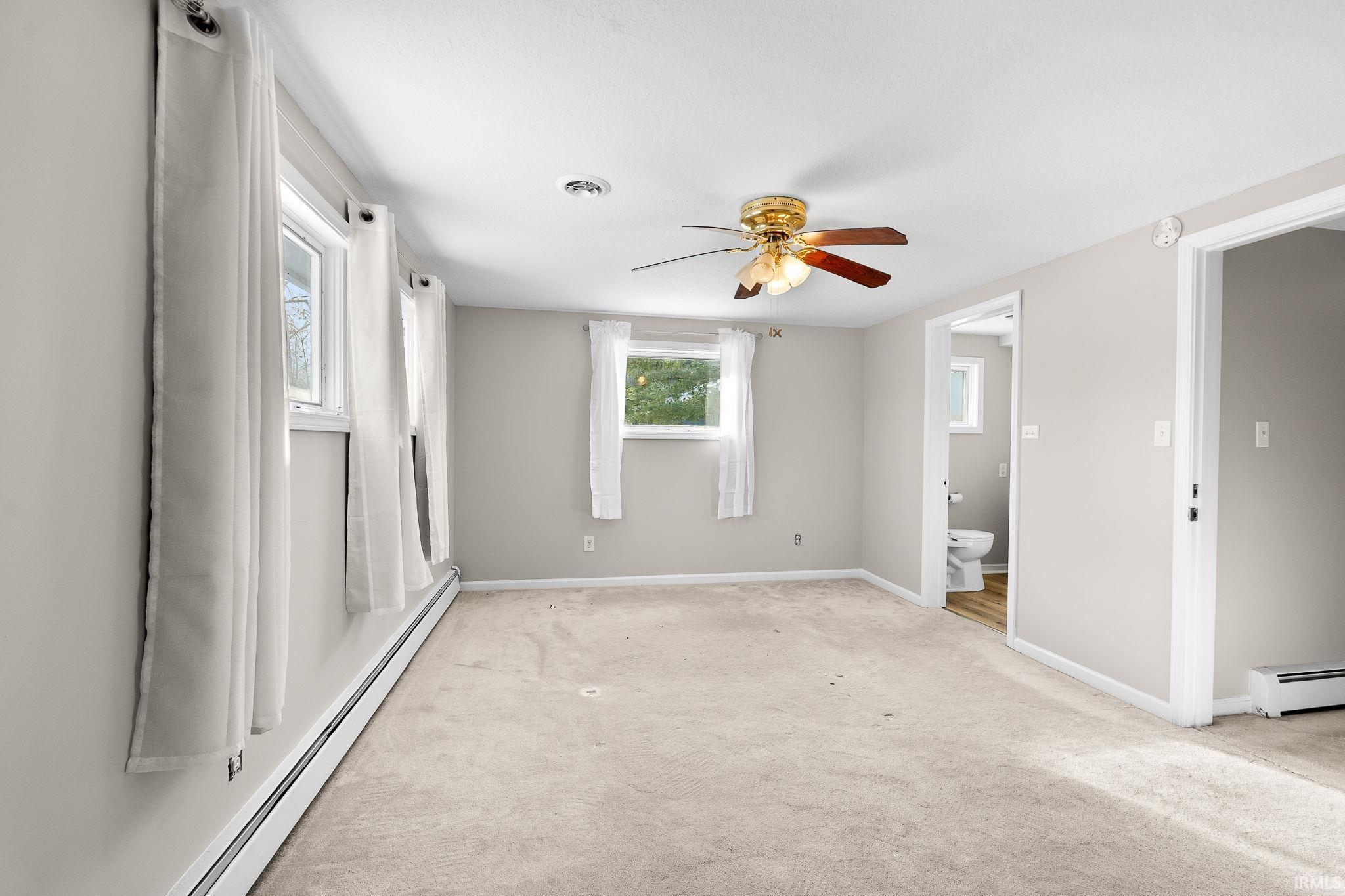 Unfurnished bedroom with baseboard heating, light carpet, a ceiling fan, and ensuite bathroom
