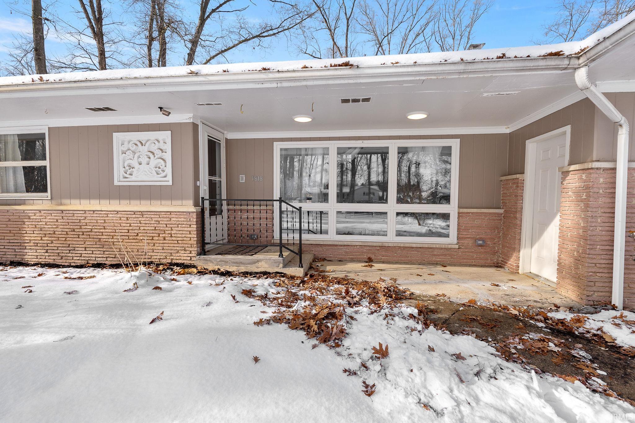 Snow covered property entrance with a patio and brick siding