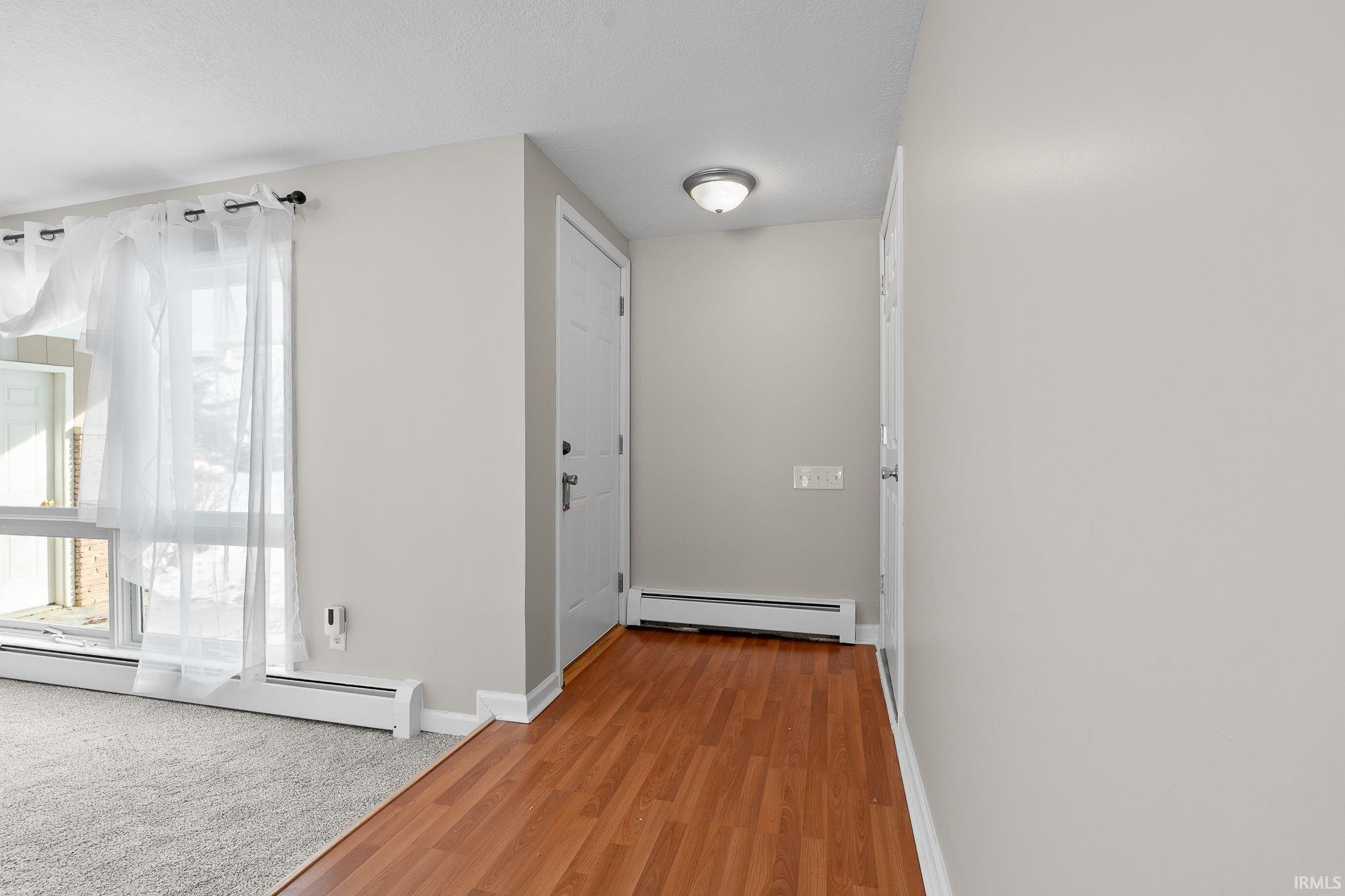 Hallway featuring baseboard heating, light wood finished floors, and light colored carpet