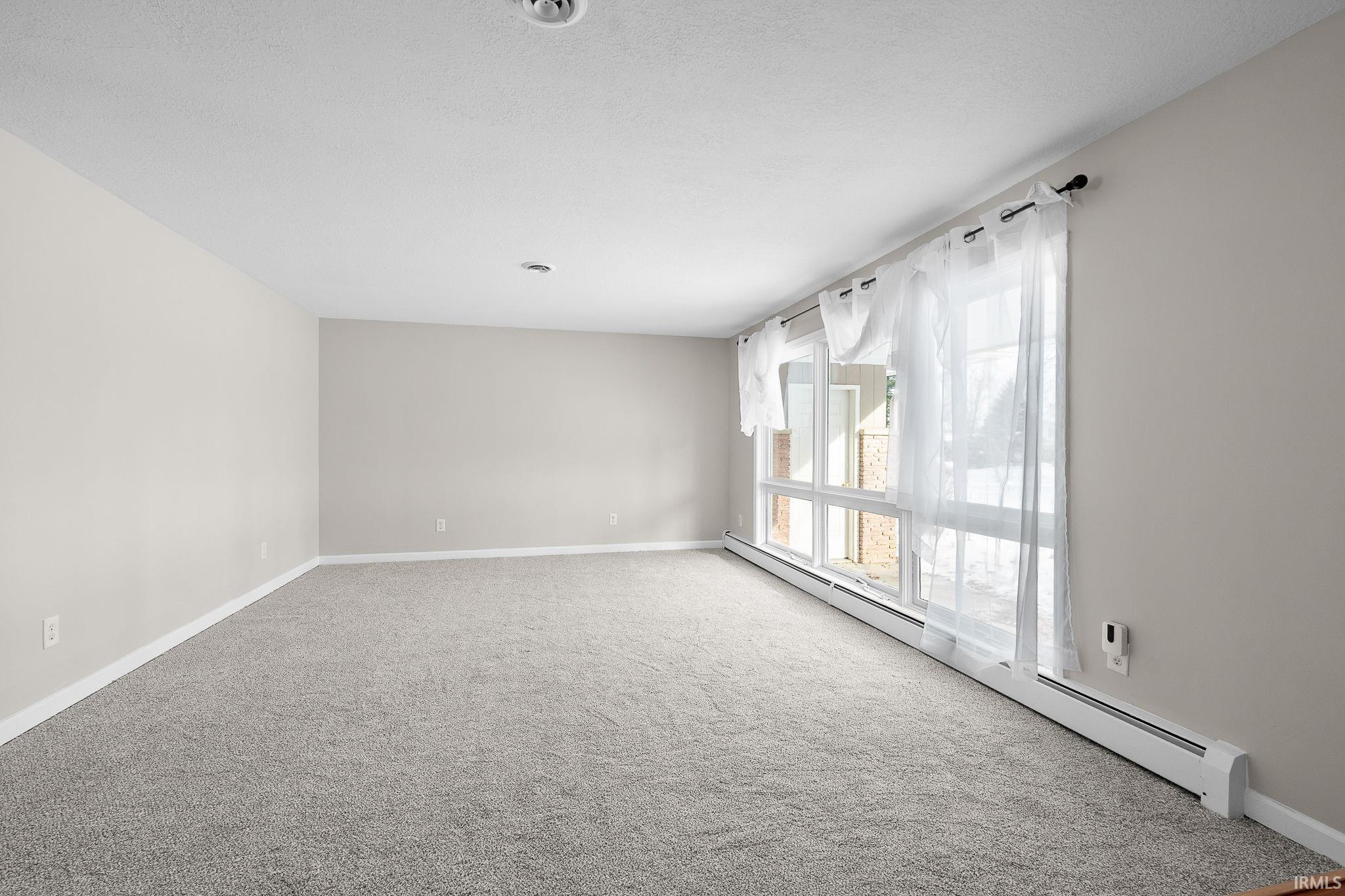 Carpeted spare room featuring a baseboard heating unit and baseboards