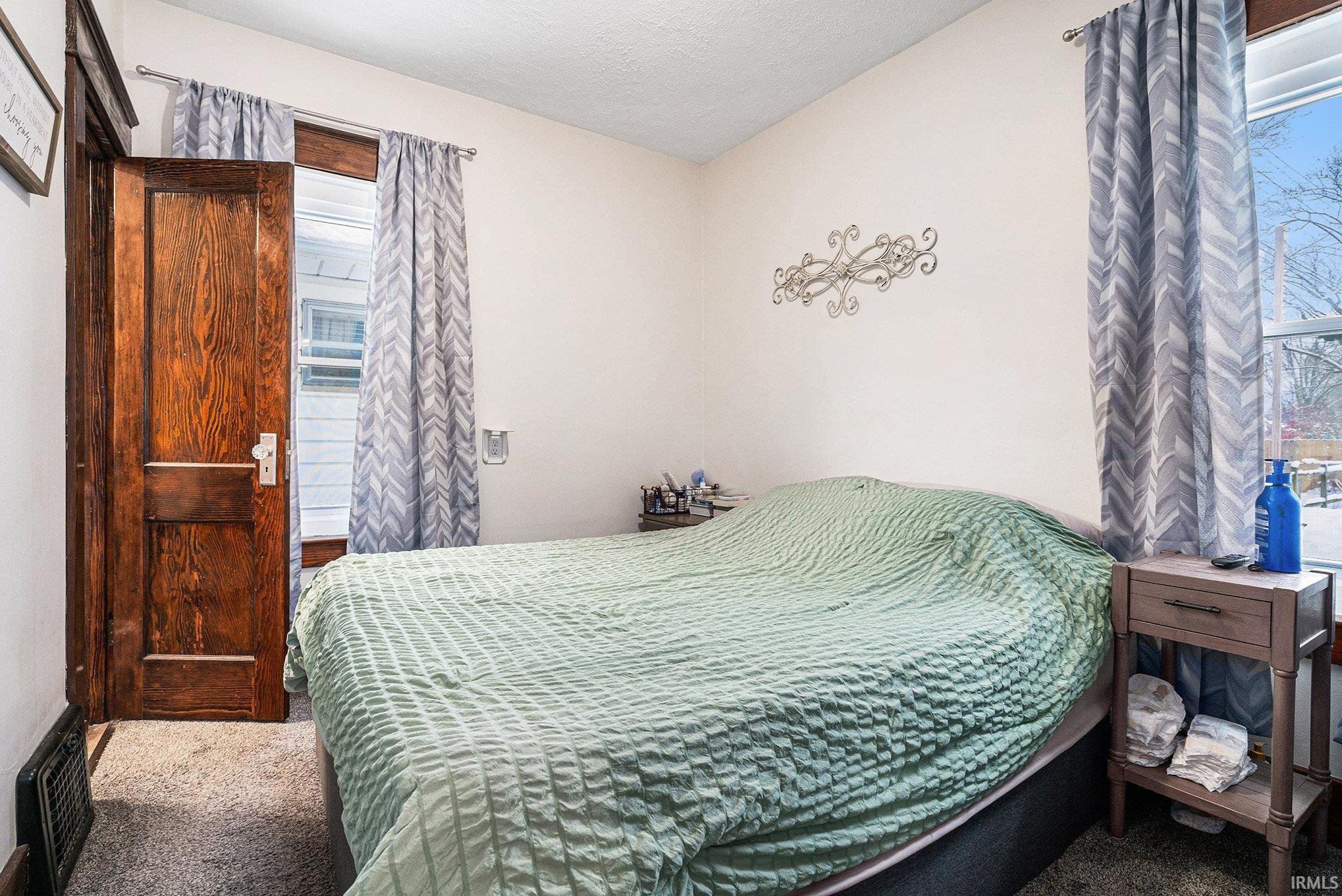 Carpeted bedroom with heating unit and multiple windows