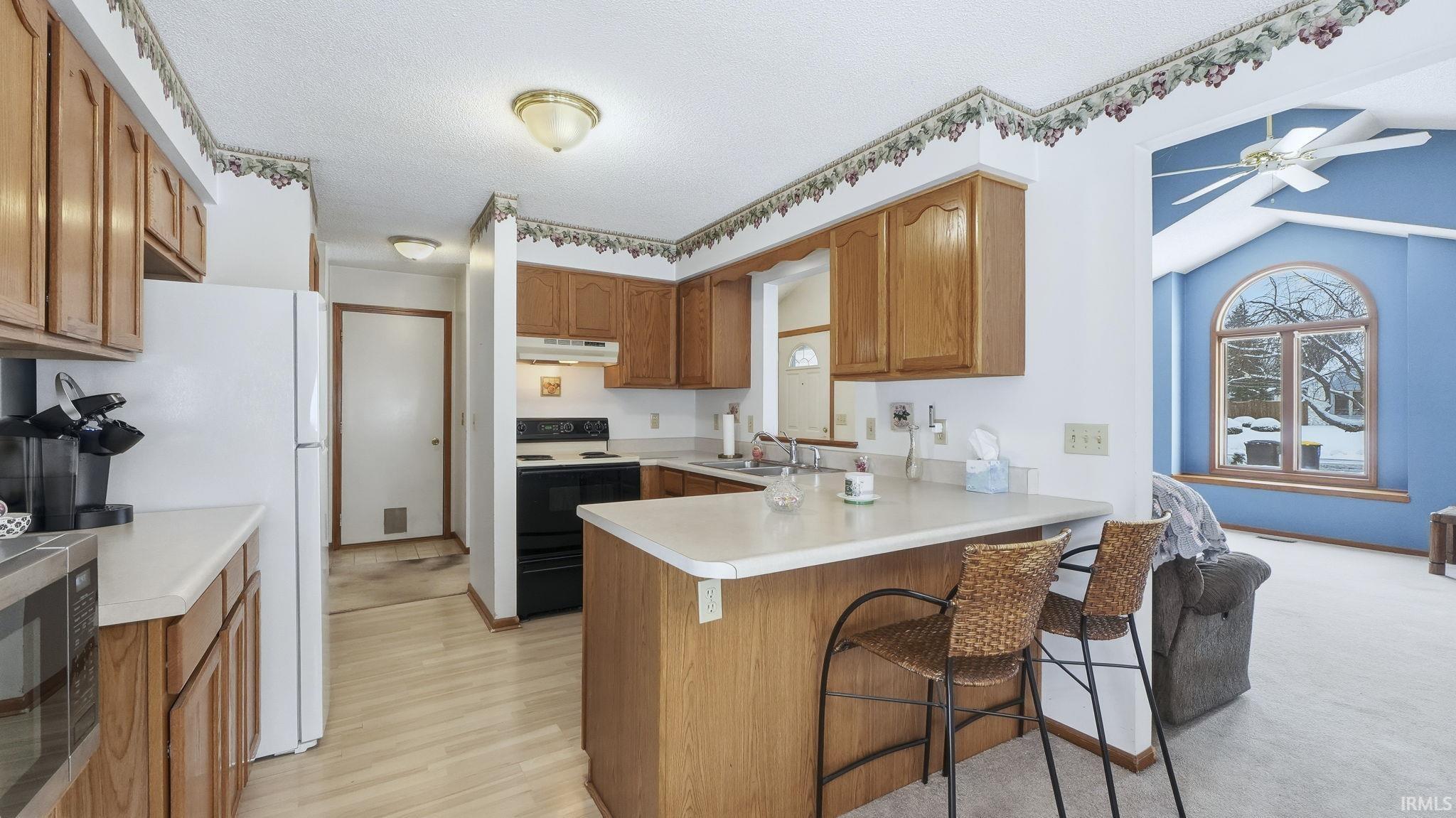 Kitchen with brown cabinetry, a kitchen bar, stainless steel microwave, electric range, and light countertops
