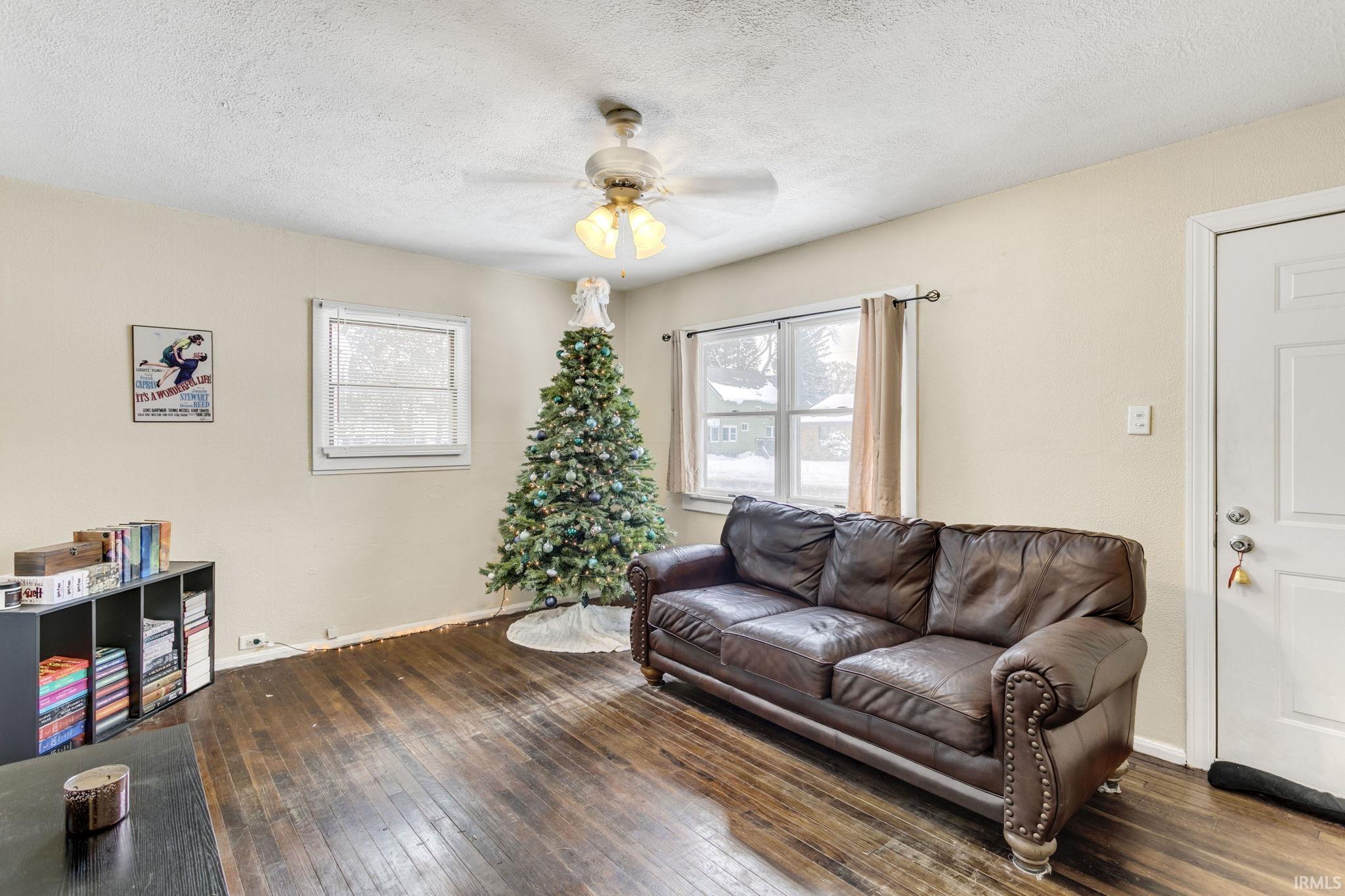 Living room with dark wood-style flooring, healthy amount of natural light, a textured ceiling, and a ceiling fan