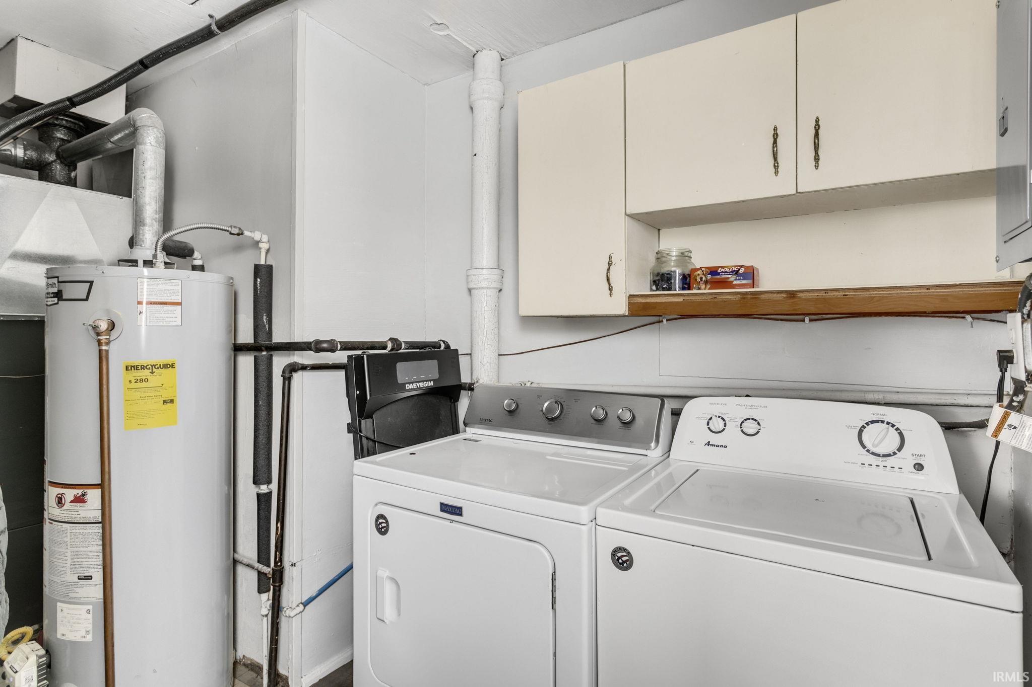 Washroom featuring cabinet space, water heater, and washing machine and dryer