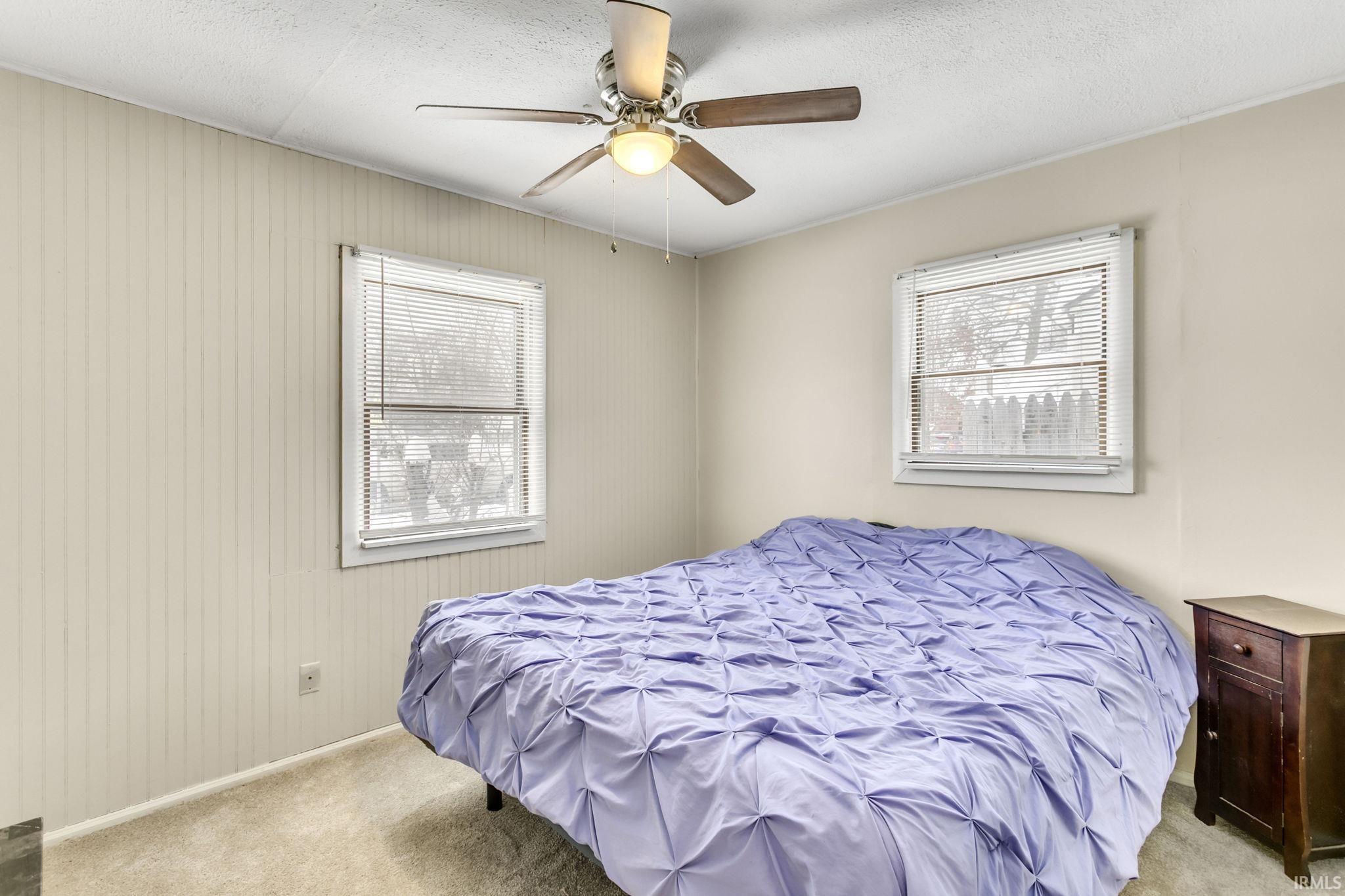 Bedroom featuring light carpet, a ceiling fan, multiple windows, and a textured ceiling