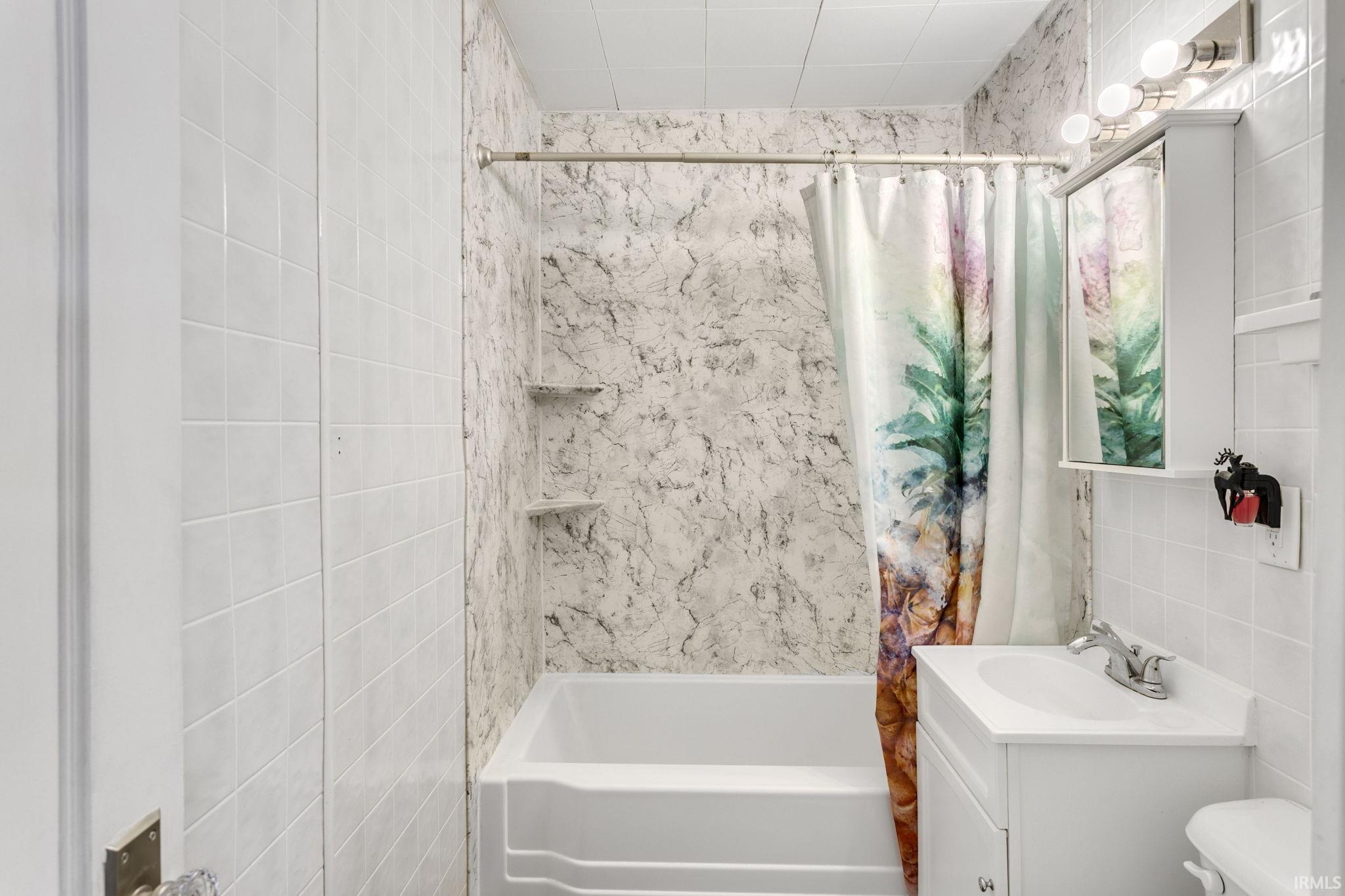 Bathroom with tile walls, shower / tub combo with curtain, and vanity