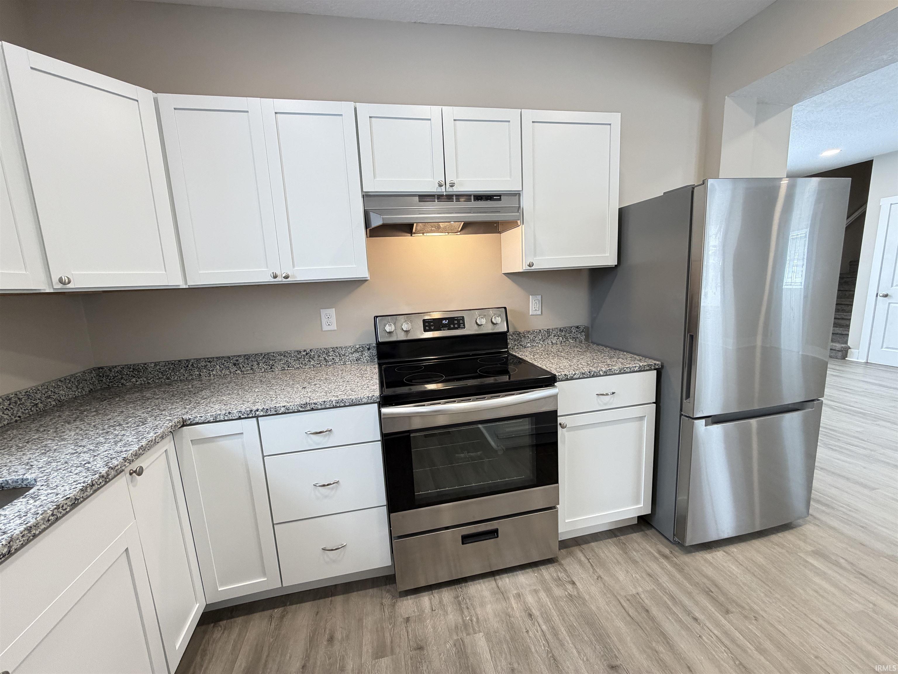 Kitchen with white cabinetry, stainless steel appliances, and light stone counters