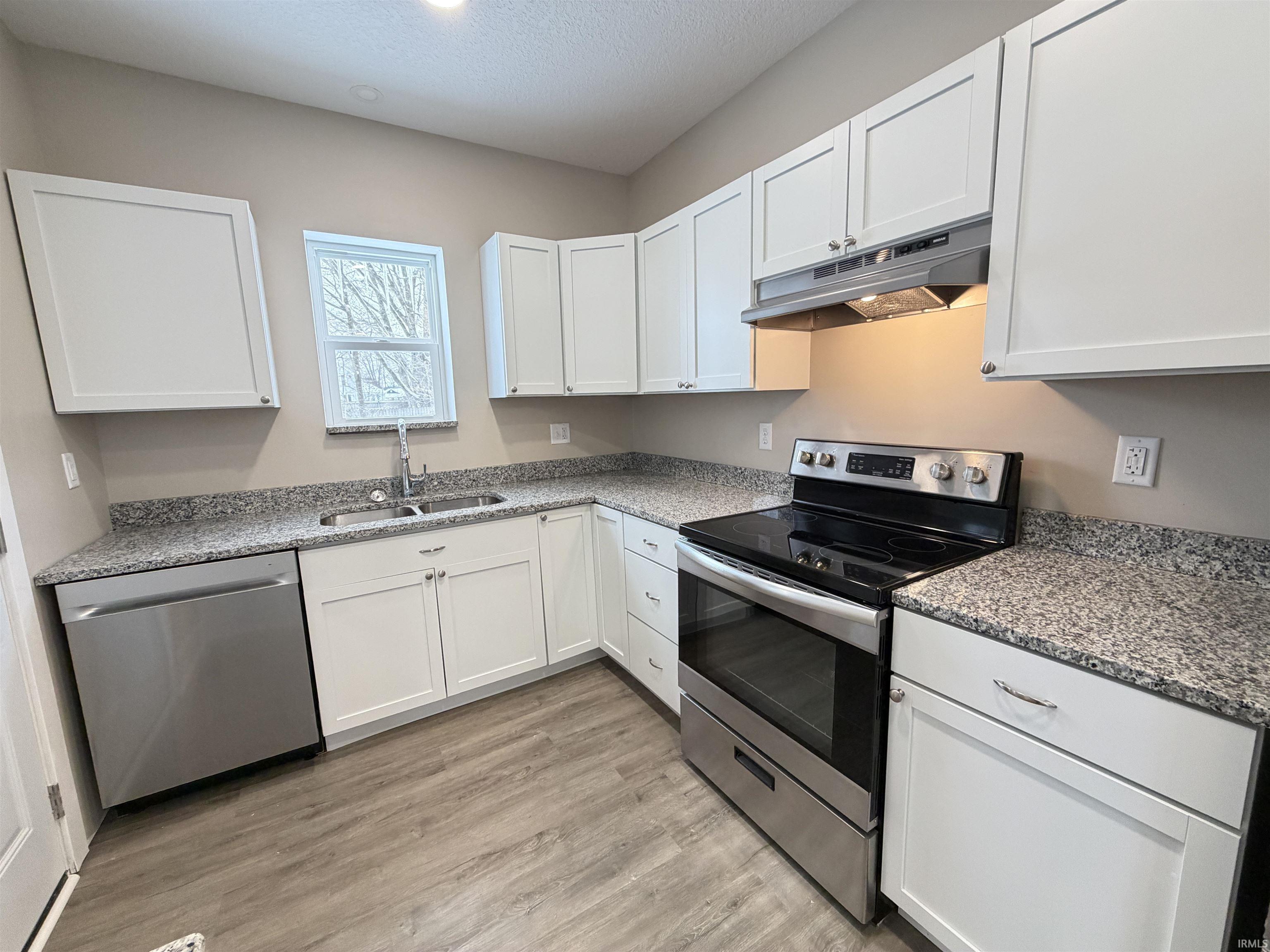 Kitchen with stainless steel appliances, white cabinetry, under cabinet range hood, light stone counters, and a textured ceiling