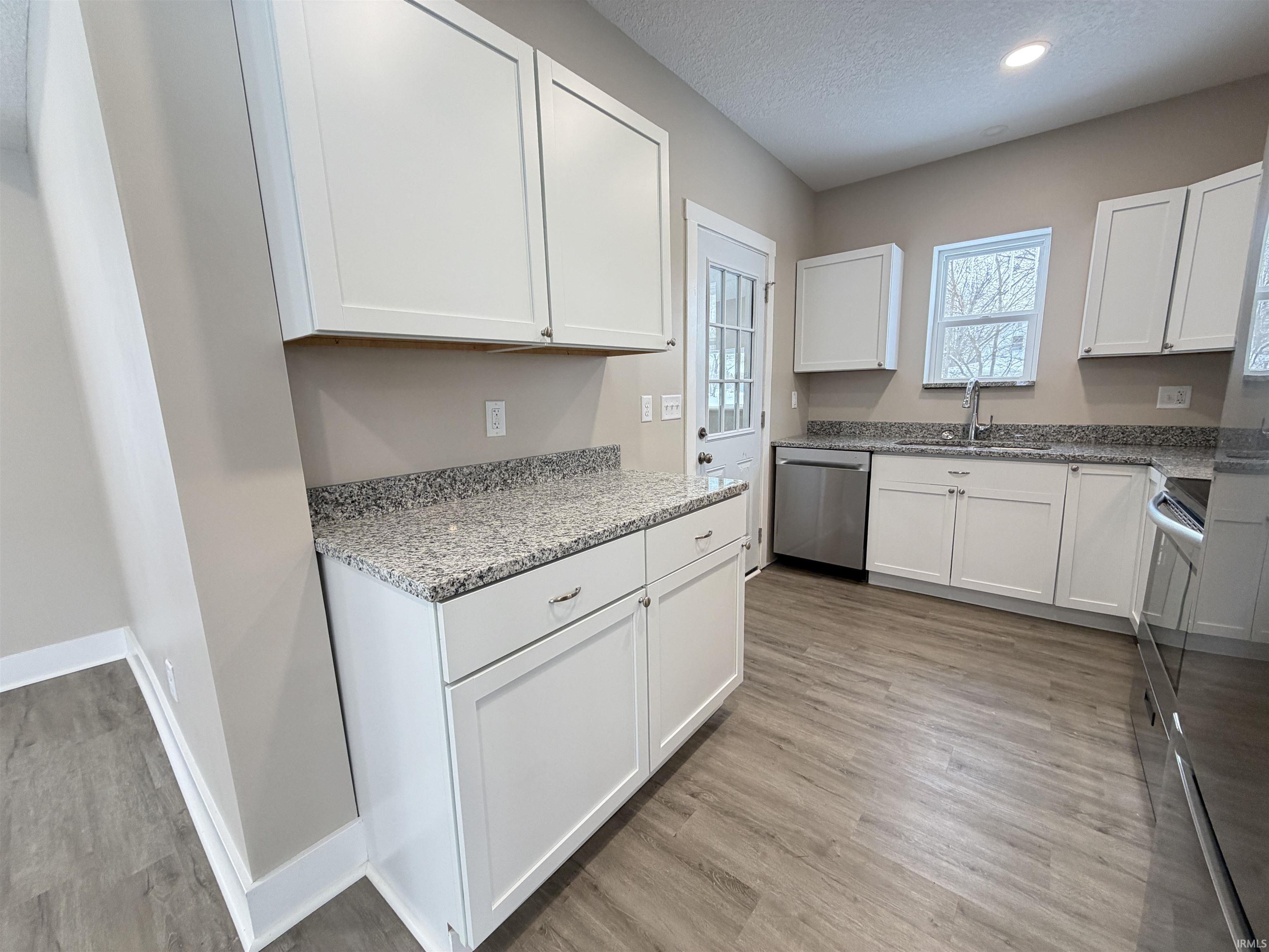 Kitchen featuring white cabinets, light stone counters, a textured ceiling, appliances with stainless steel finishes, and light wood finished floors