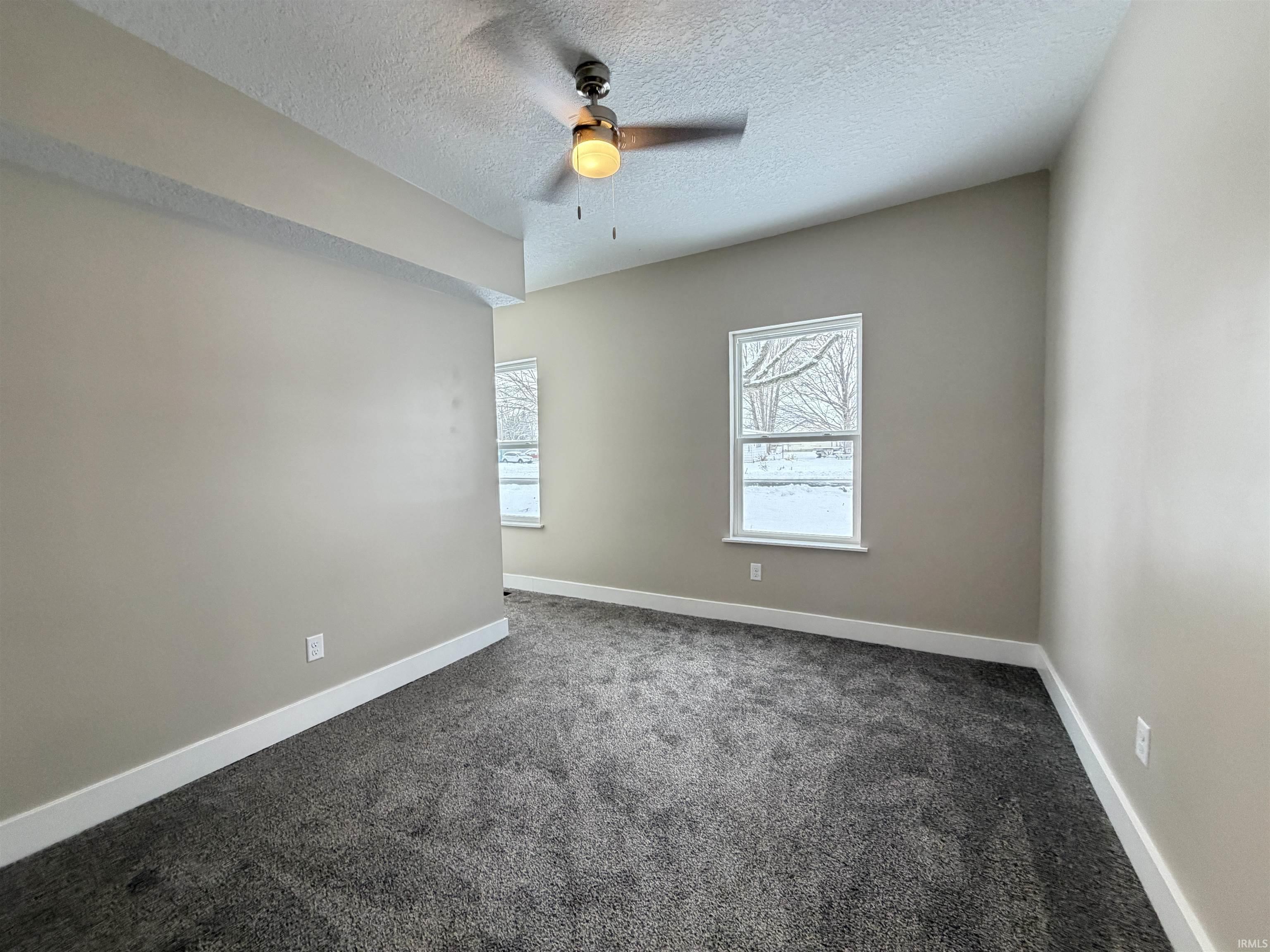 Spare room featuring a textured ceiling, dark colored carpet, and a ceiling fan