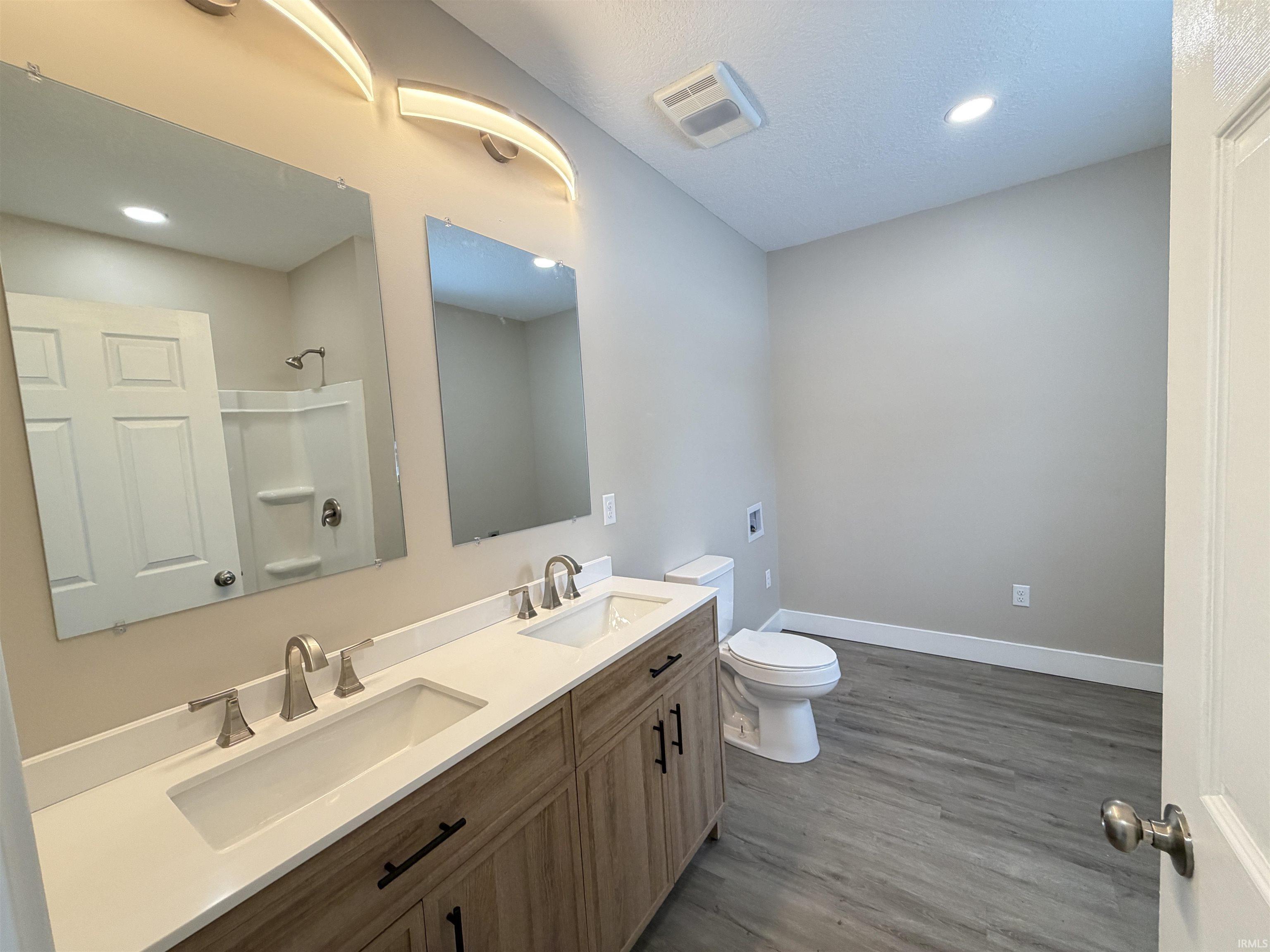 Bathroom with double vanity, a shower, dark wood-type flooring, and recessed lighting