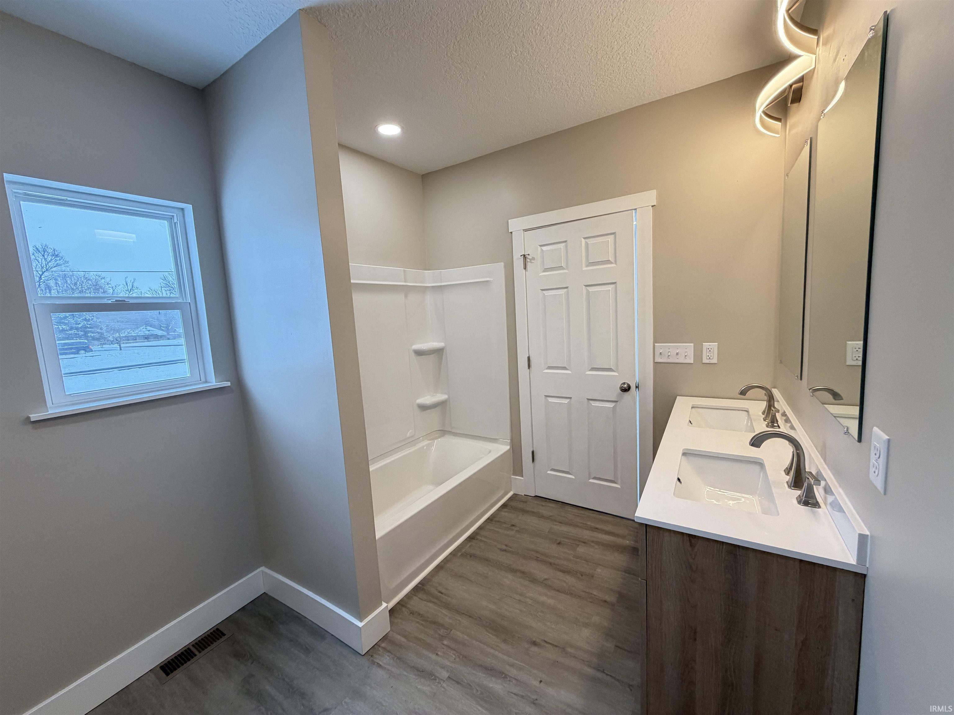 Full bathroom with double vanity, dark wood-type flooring, a textured ceiling, and shower / bath combination