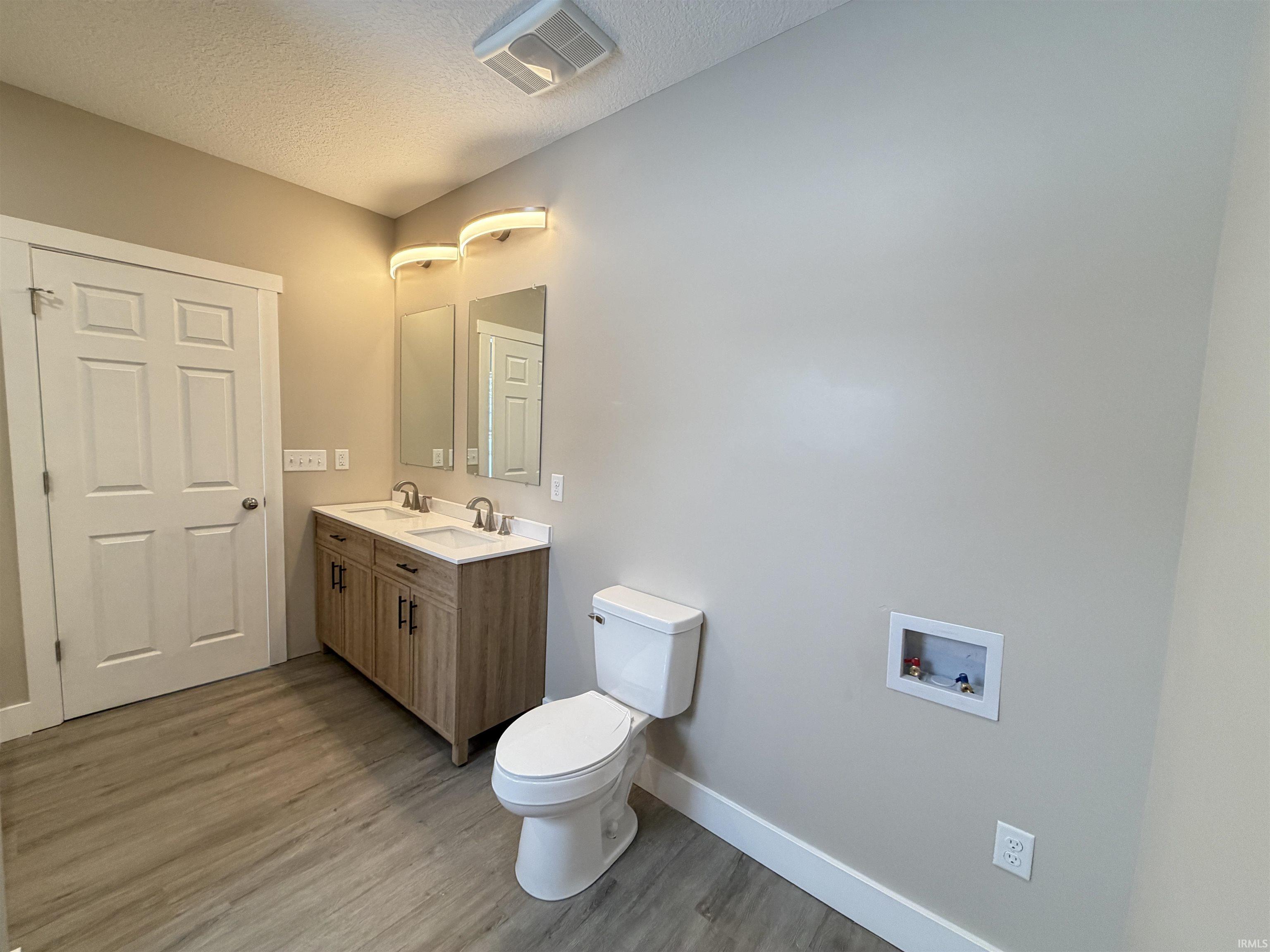 Bathroom featuring double vanity, a textured ceiling, and light wood-style flooring