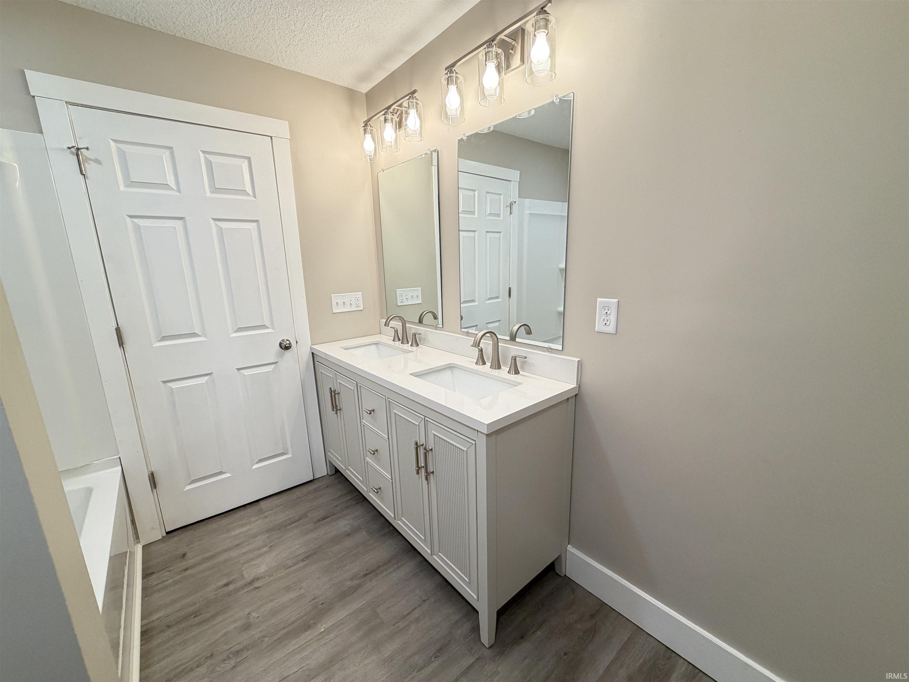 Full bathroom with double vanity, dark wood-style floors, and a textured ceiling