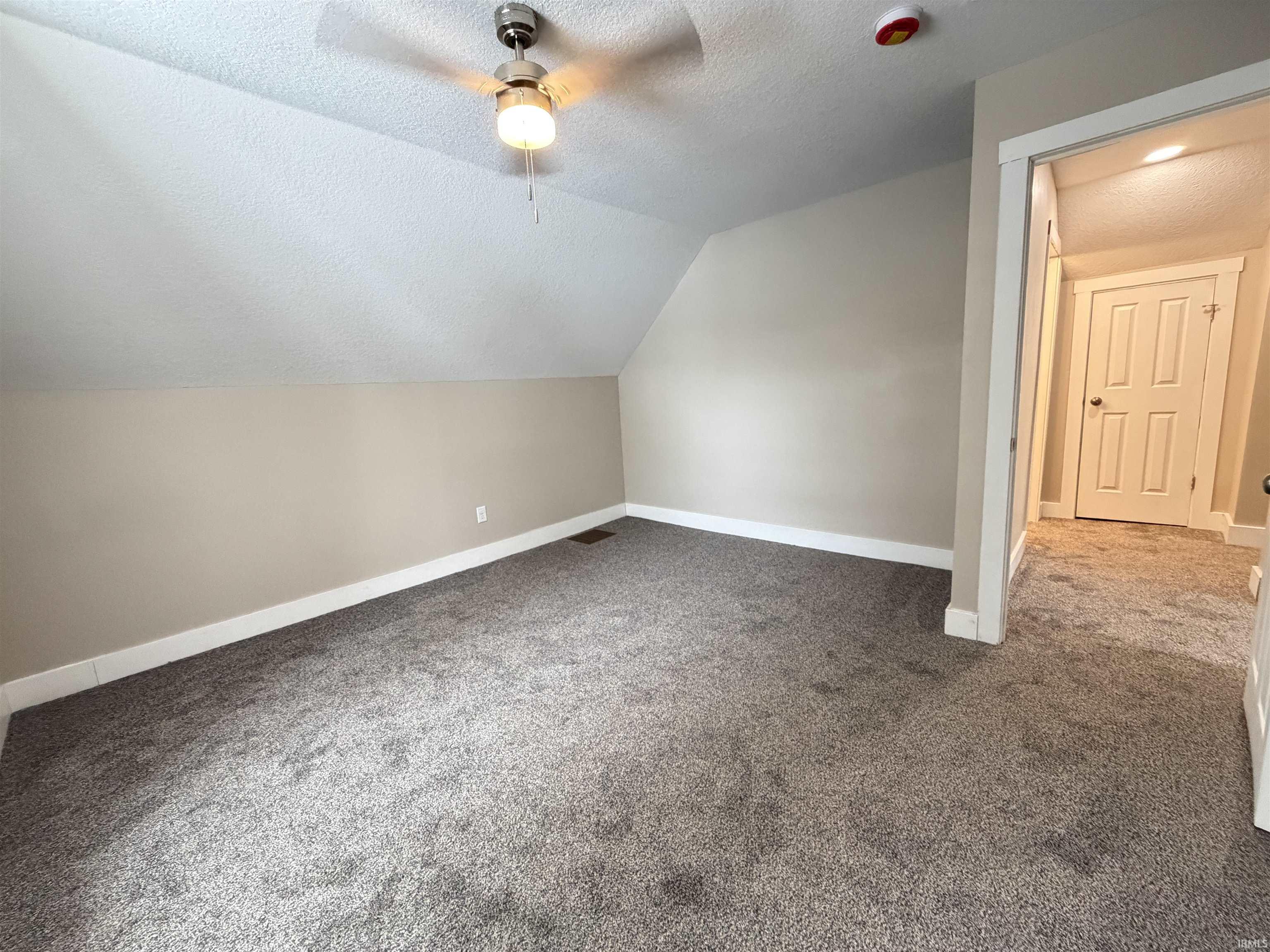Additional living space with a textured ceiling, lofted ceiling, carpet, and ceiling fan