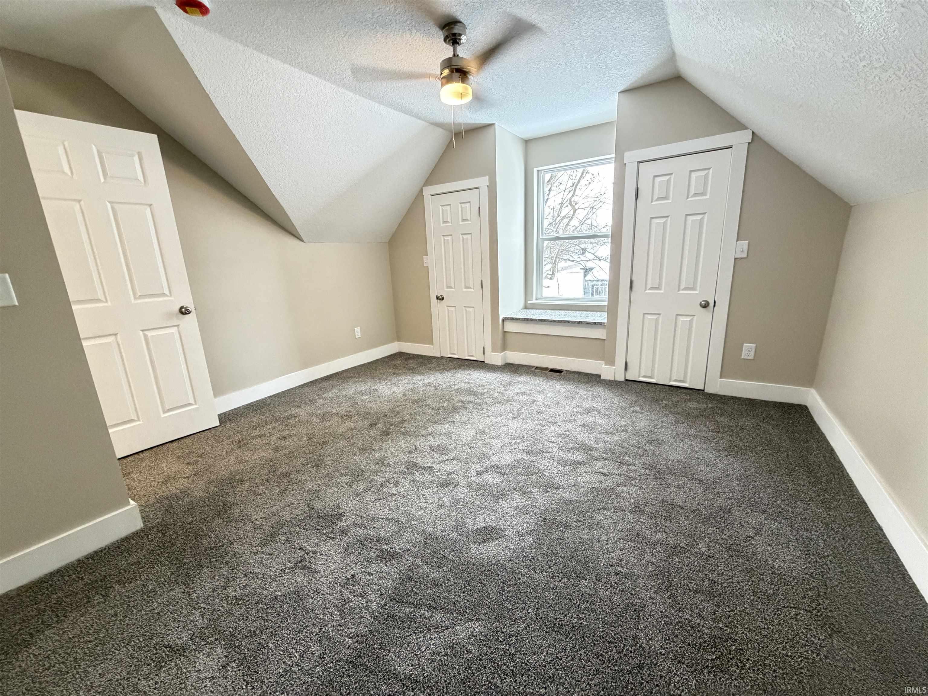 Bonus room with a textured ceiling, vaulted ceiling, dark carpet, and a ceiling fan