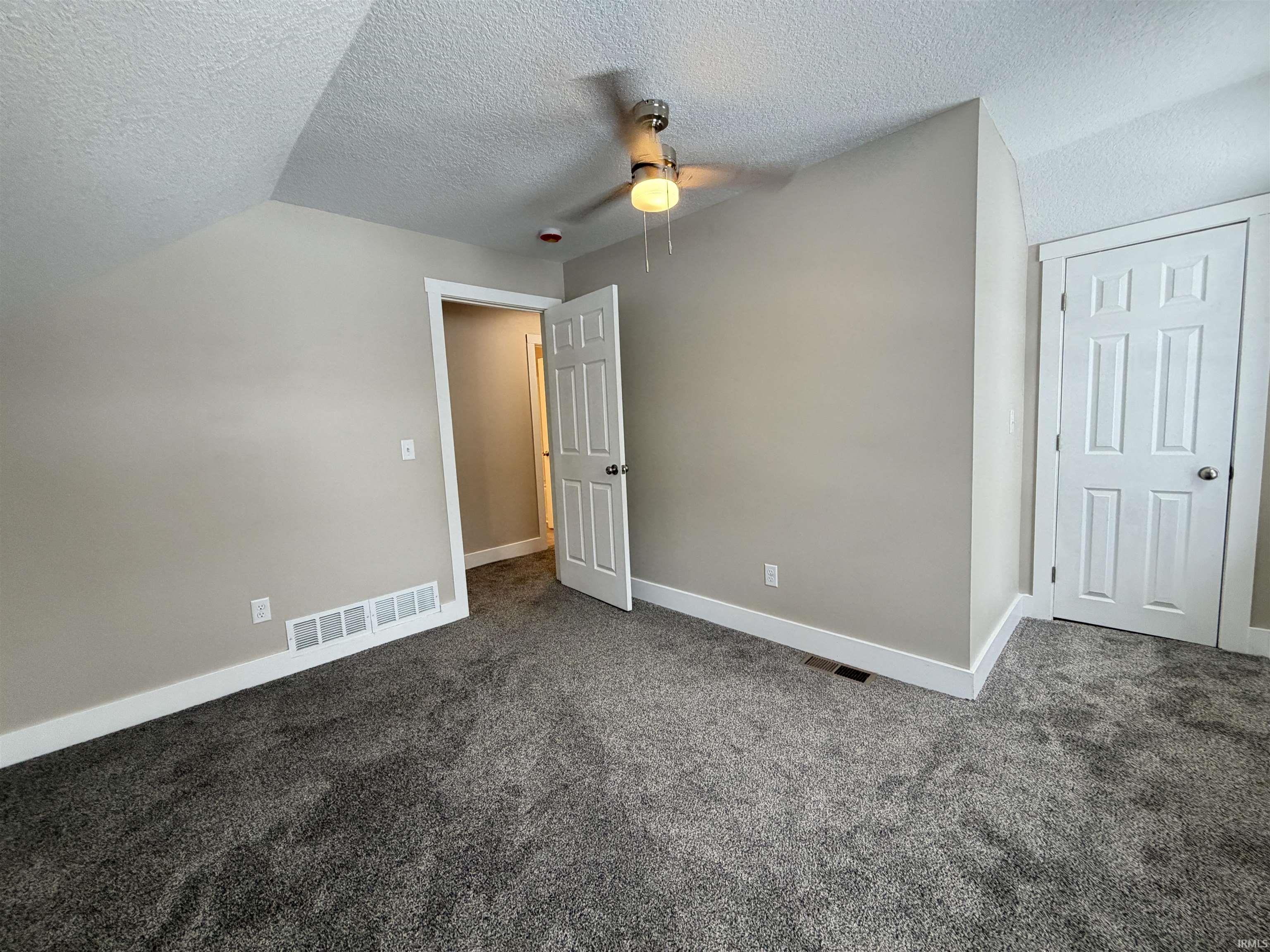Unfurnished bedroom with a textured ceiling, dark carpet, and vaulted ceiling