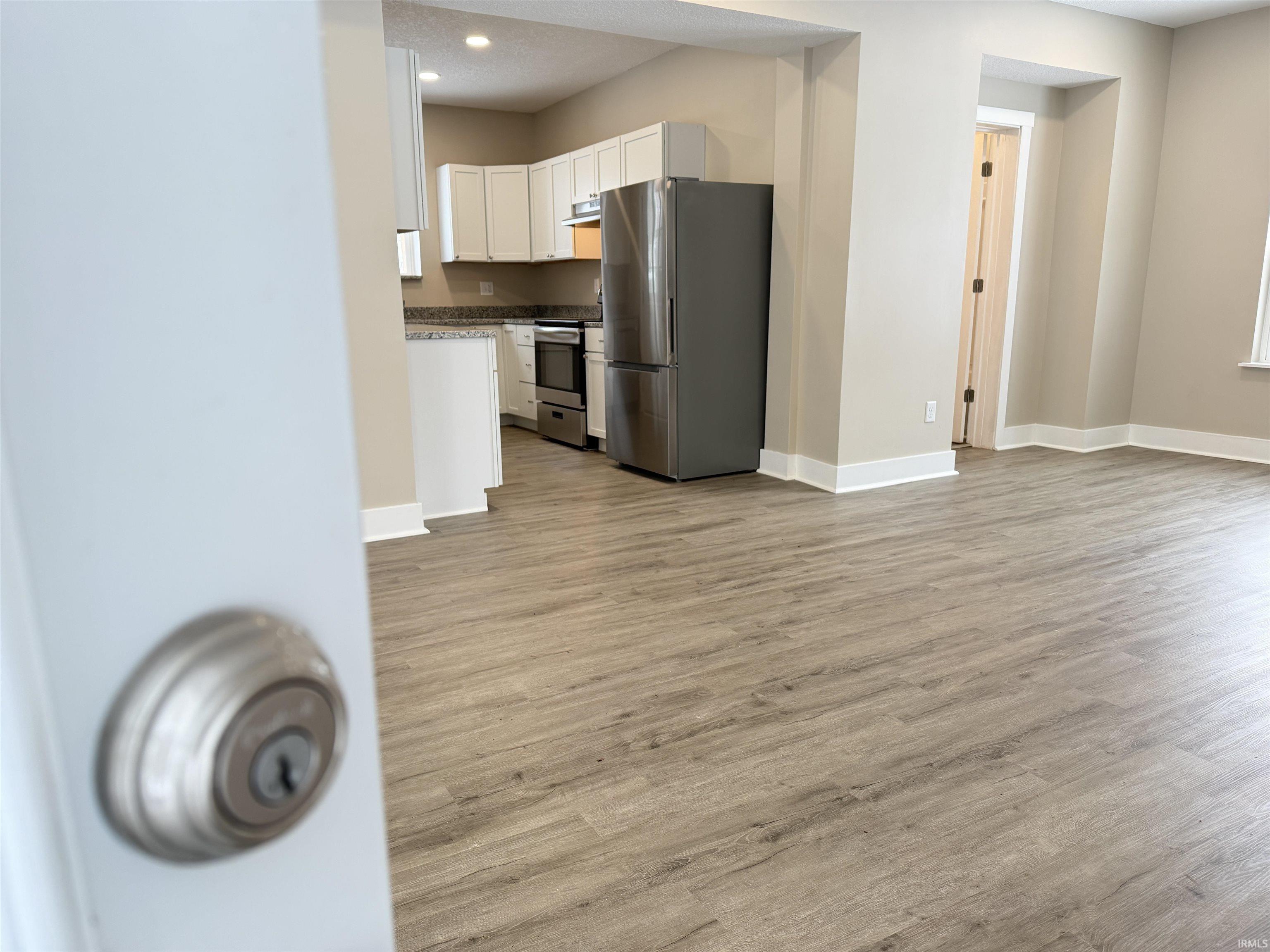 Kitchen with appliances with stainless steel finishes, white cabinets, light wood finished floors, under cabinet range hood, and recessed lighting