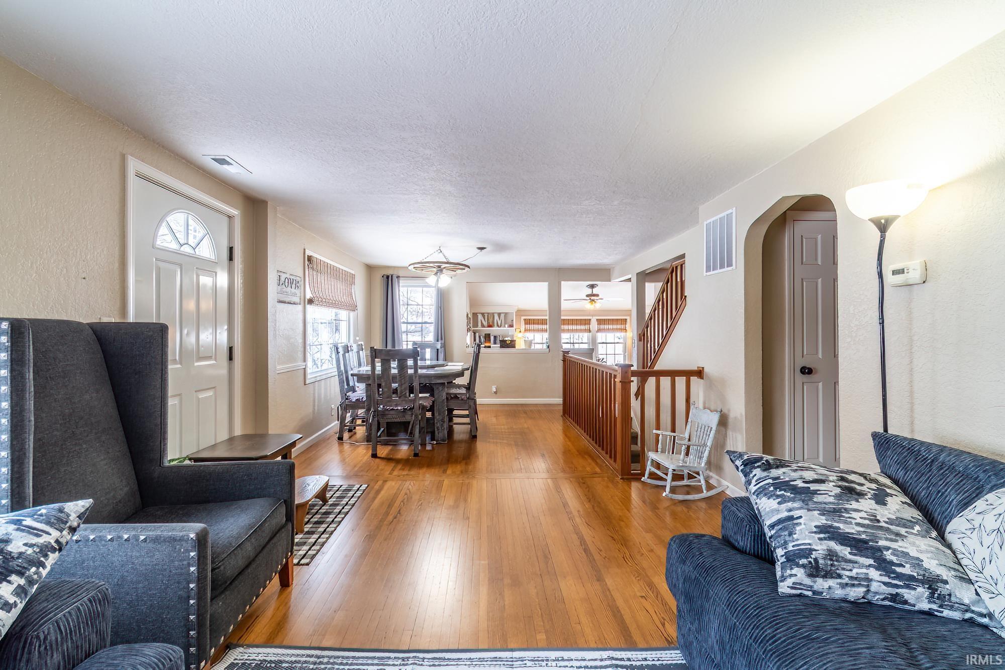 Living room featuring wood finished floors, arched walkways, a textured ceiling, and a textured wall