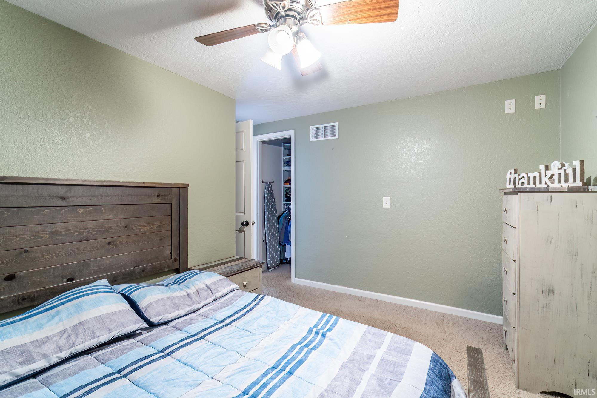 Bedroom featuring a textured wall, a spacious closet, a textured ceiling, light colored carpet, and ceiling fan