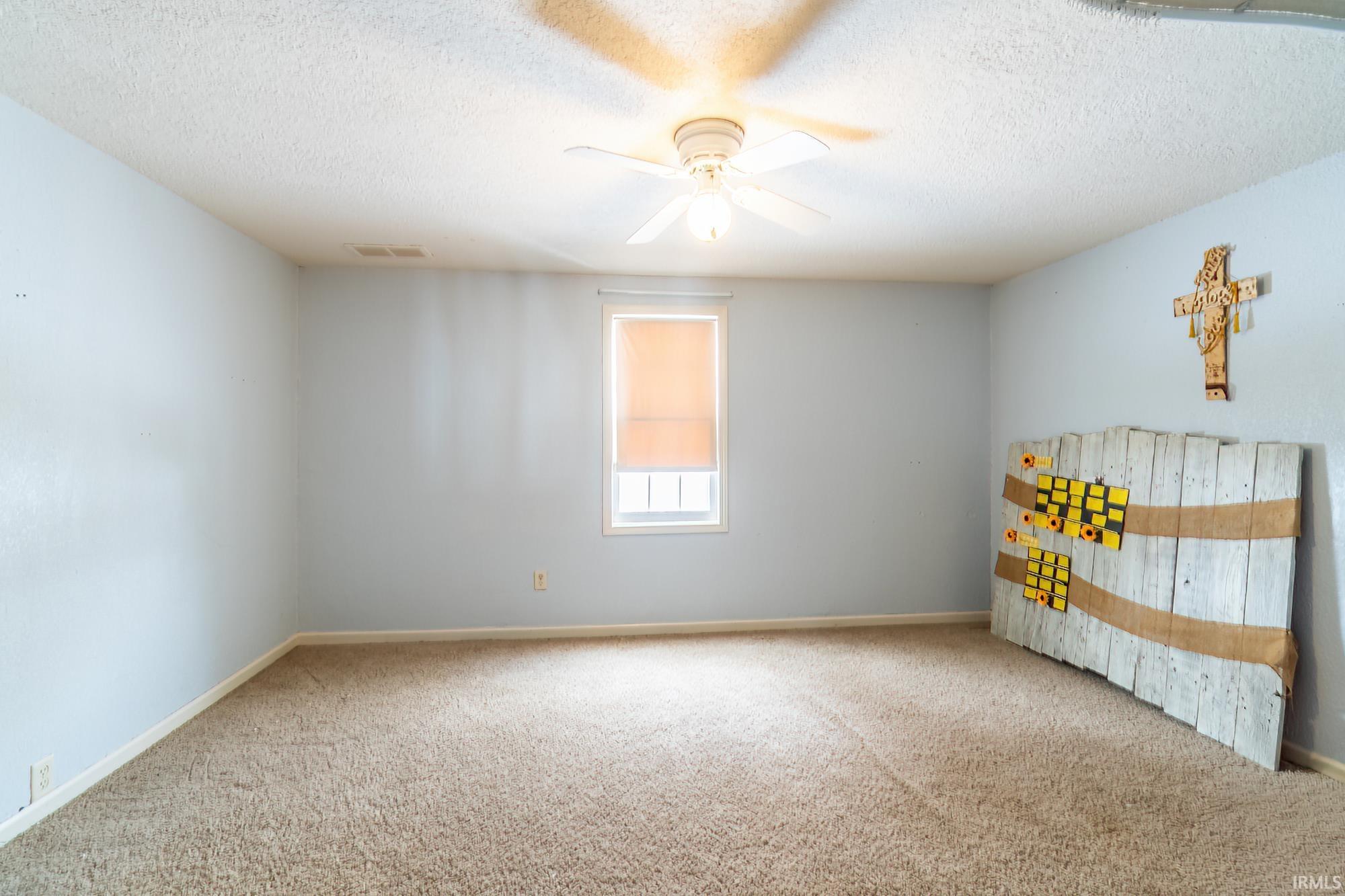 Empty room with a textured ceiling, carpet flooring, and a ceiling fan